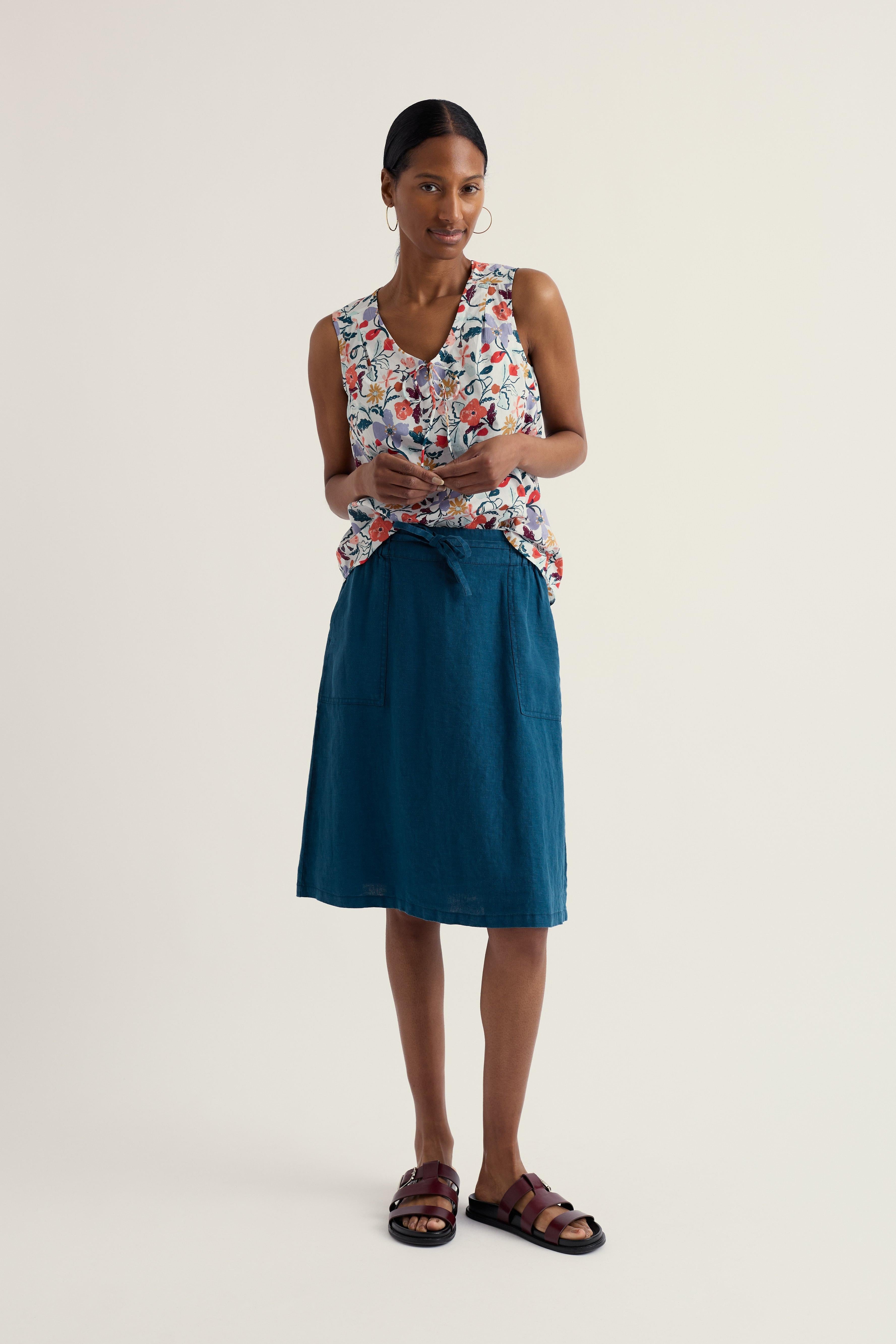 Woman wearing a floral sleeveless top and teal skirt on a plain background