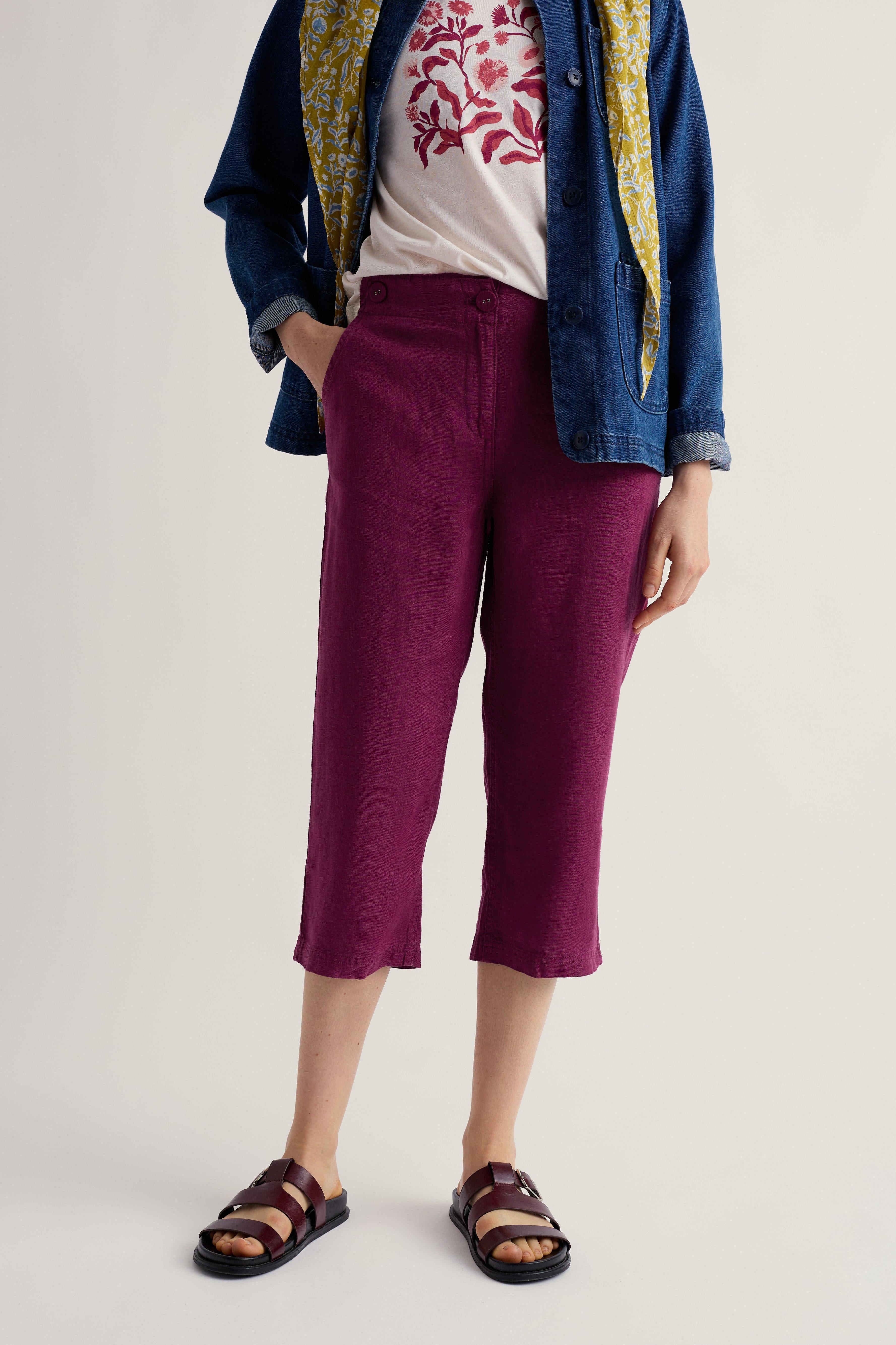 Person wearing a blue jacket, white shirt with red floral design, and purple cropped trousers on a light background