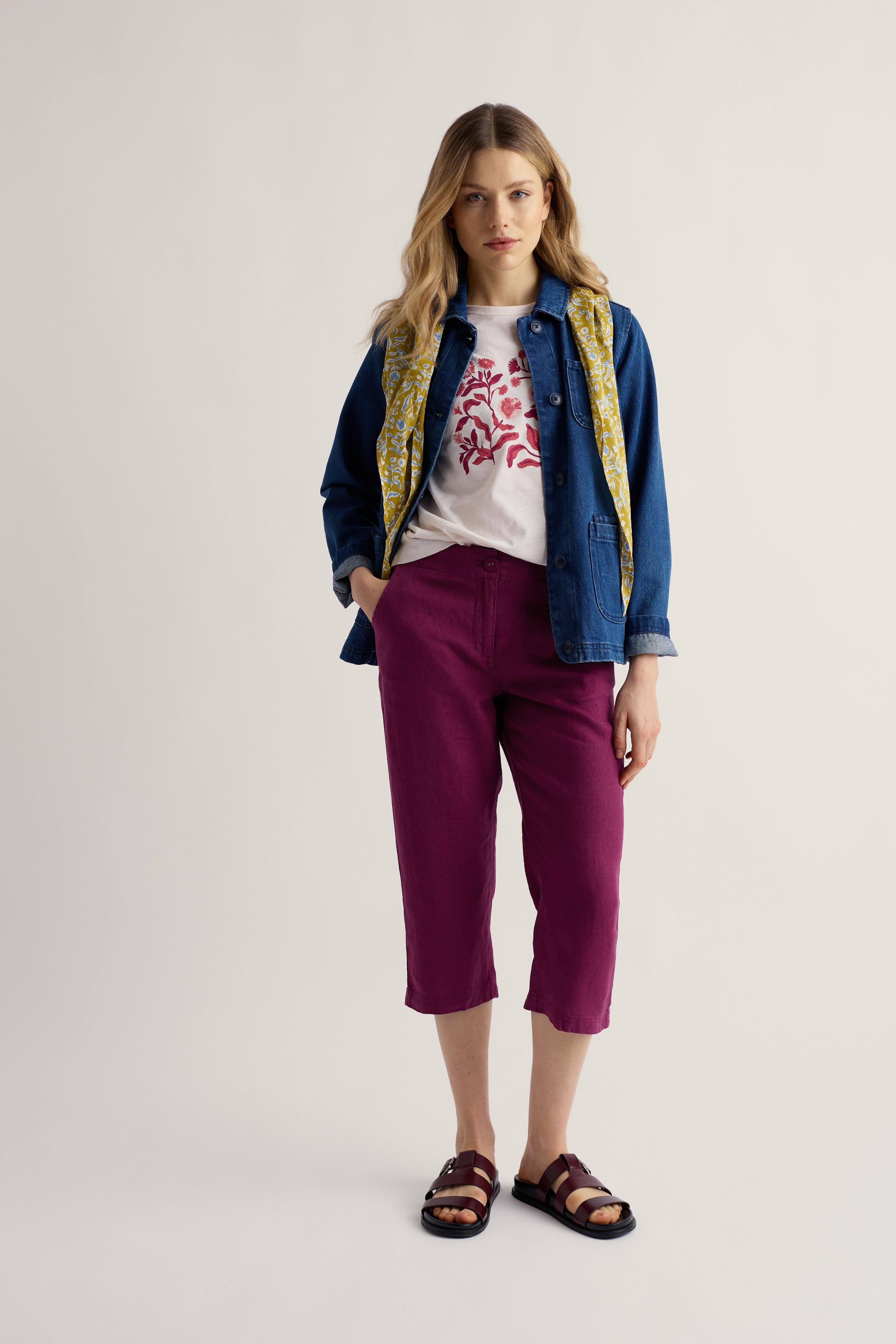 Woman wearing a denim jacket, white t-shirt with red design, and purple cropped pants on a plain background