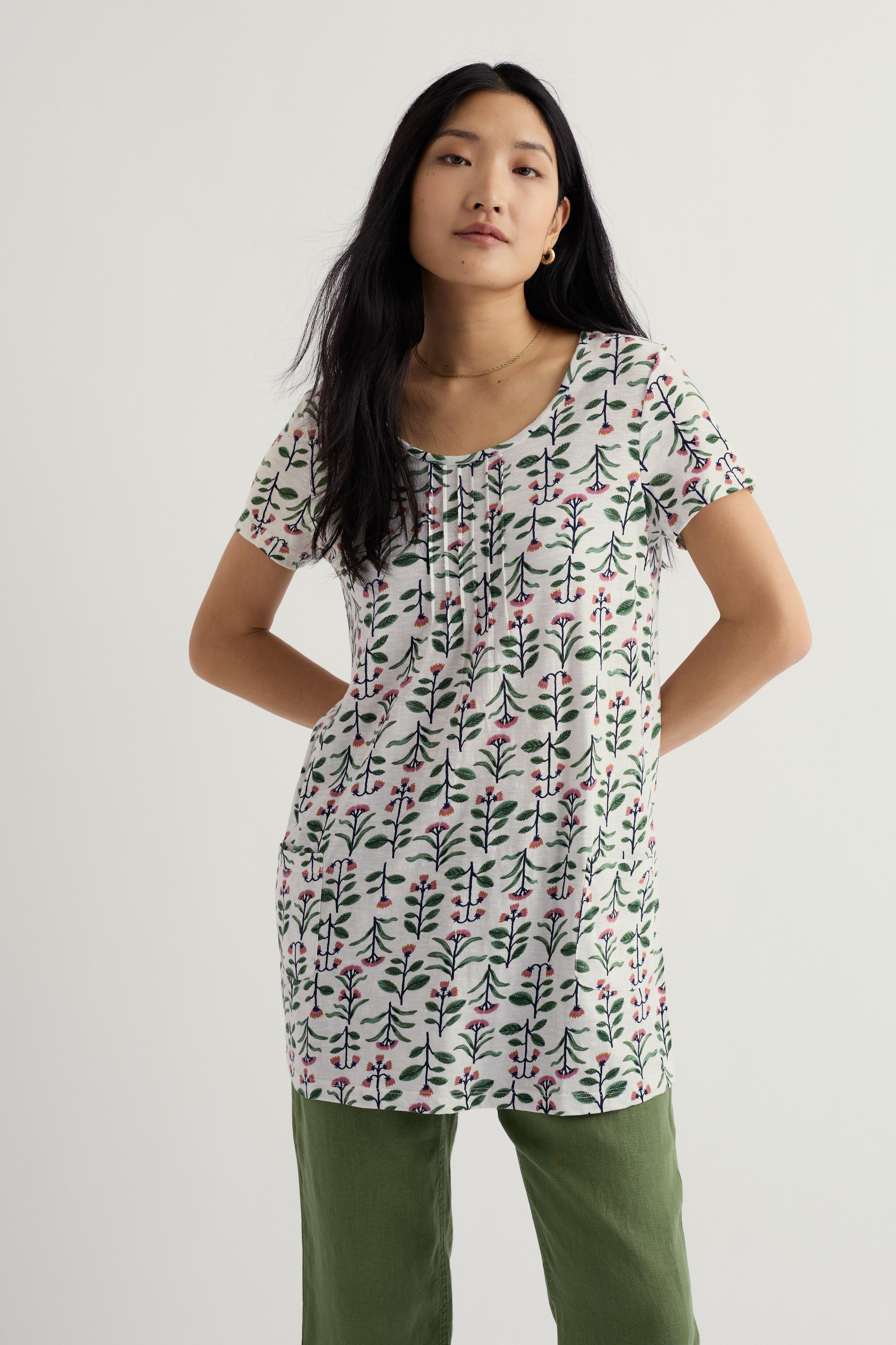 Woman wearing a floral tunic and green pants on a plain background