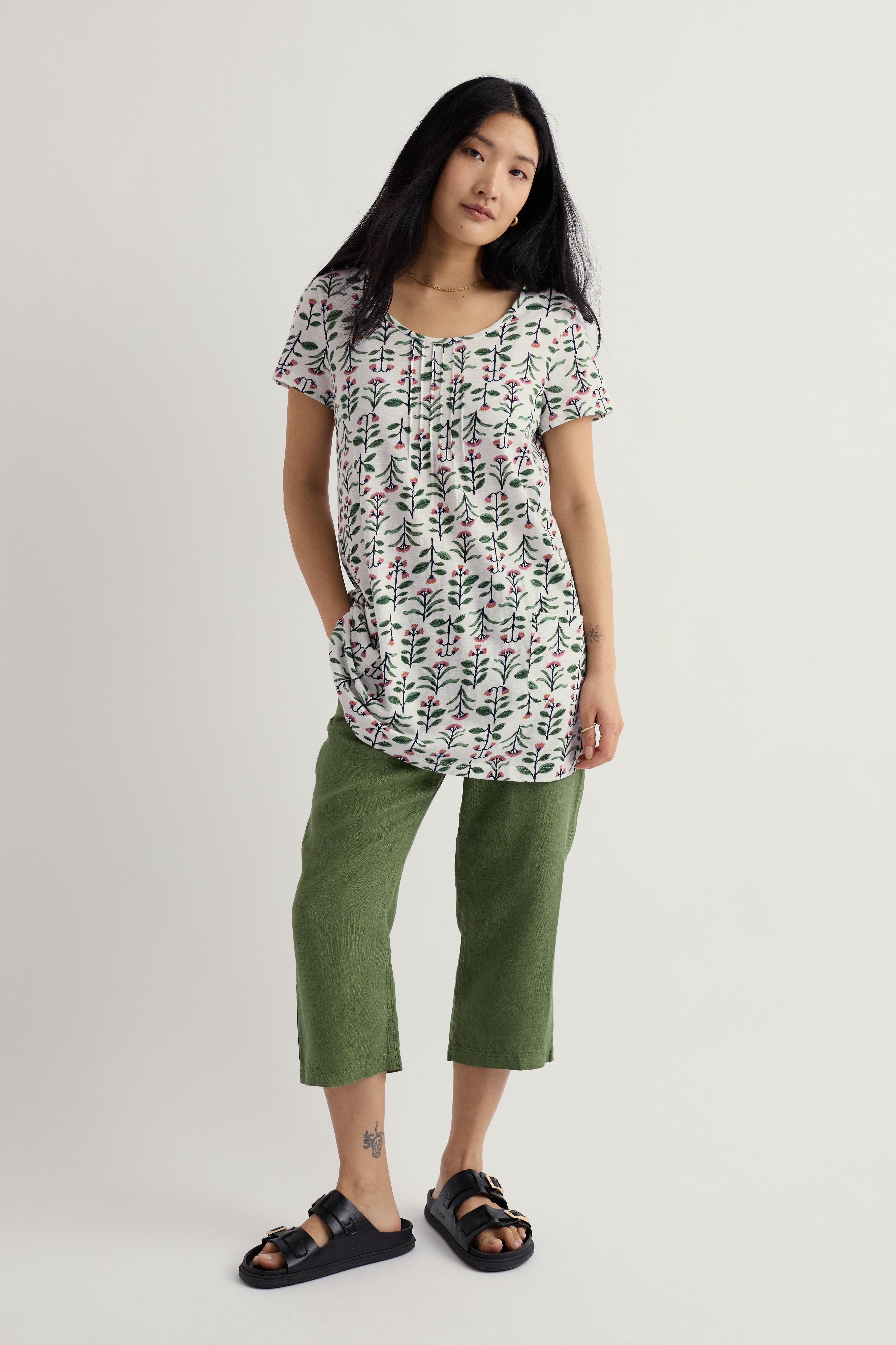Woman wearing a patterned top and green cropped pants on a white background