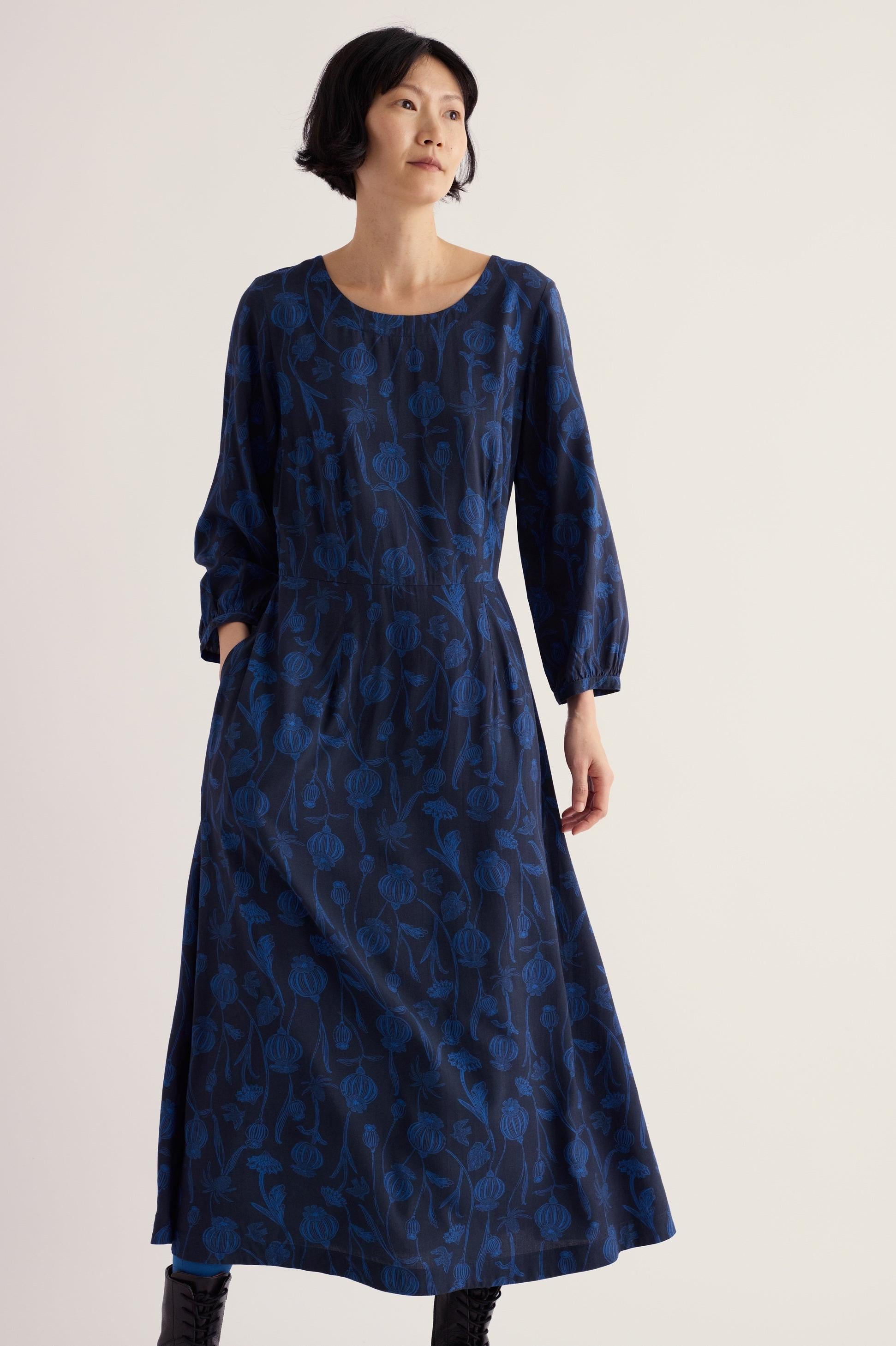 A woman wearing a blue midi-length Seasalt Cornwall floral print viscose dress against a plain background.