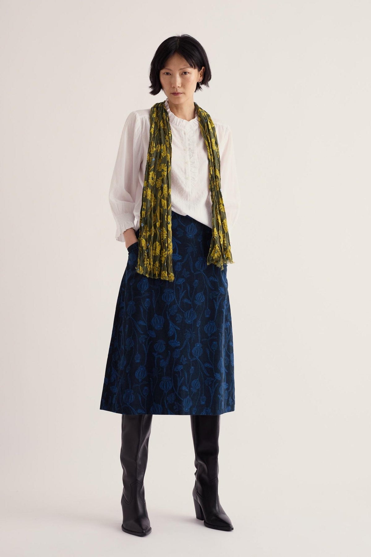 Woman wearing a Seasalt Cornwall blue patterned needlecord skirt with a white blouse and scarf.