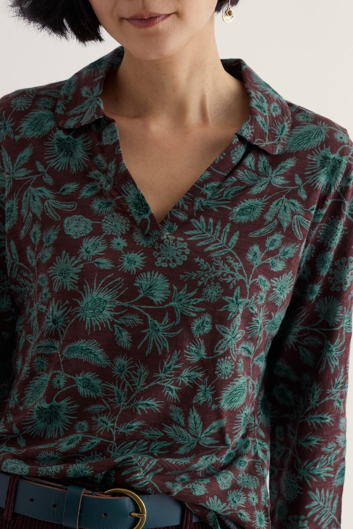 Woman wearing a brown Seasalt Cornwall long-sleeve shirt with a blue and green floral botanical print.