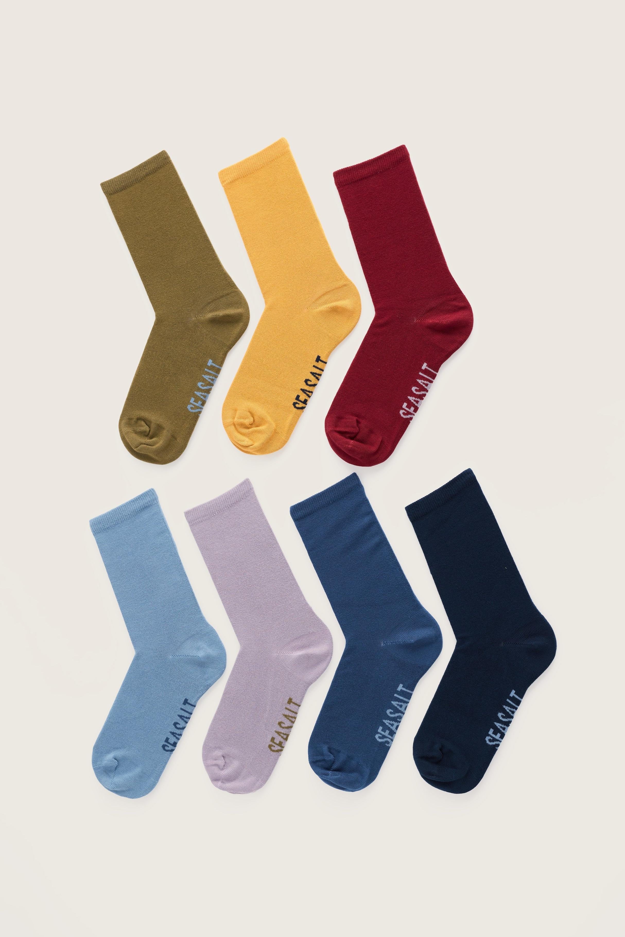 A flat lay collection of seven colorful organic cotton socks by Seasalt Cornwall arranged on a plain background.