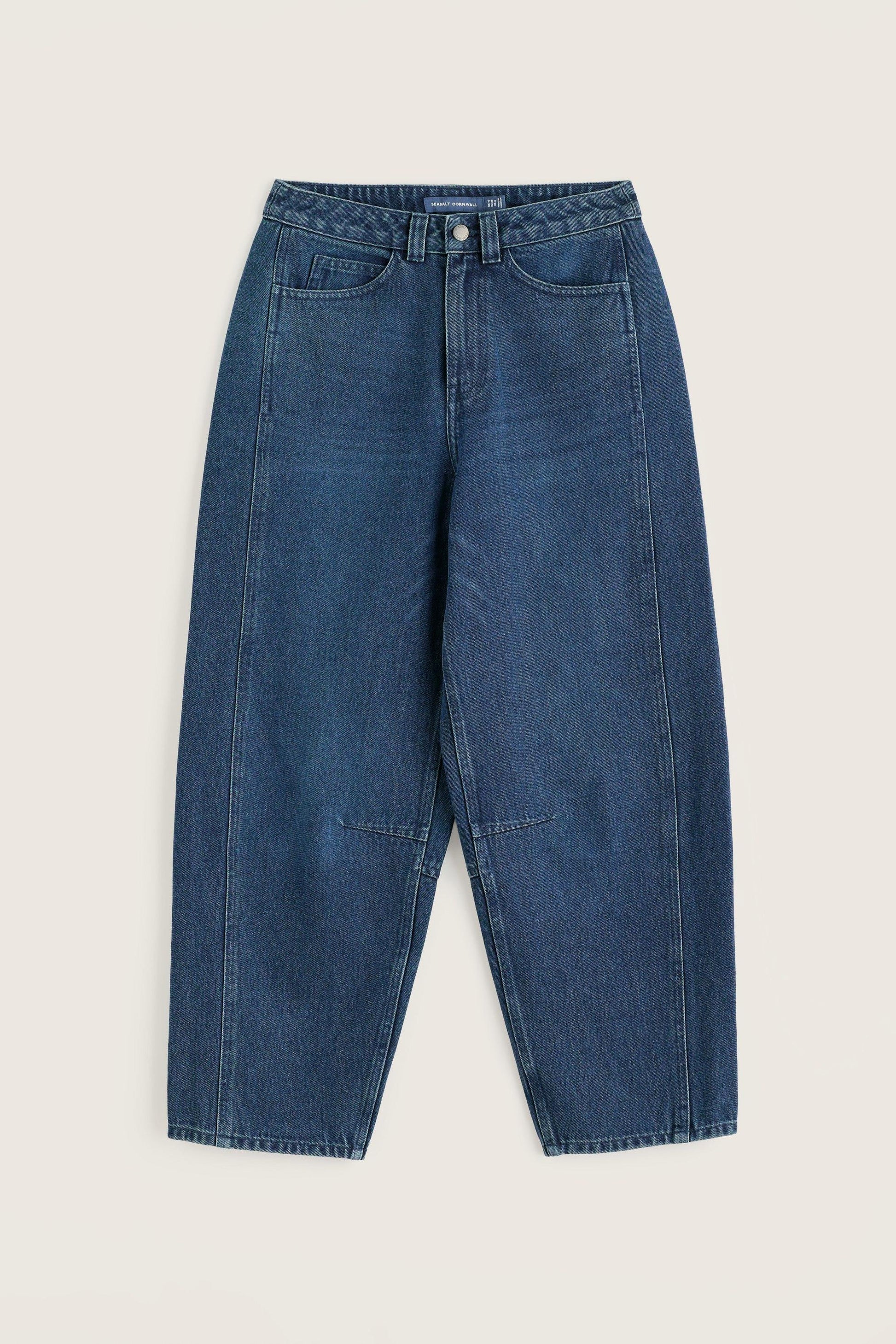 A pair of relaxed-fit blue denim jeans with a wide waistband, laid flat against a light beige background.