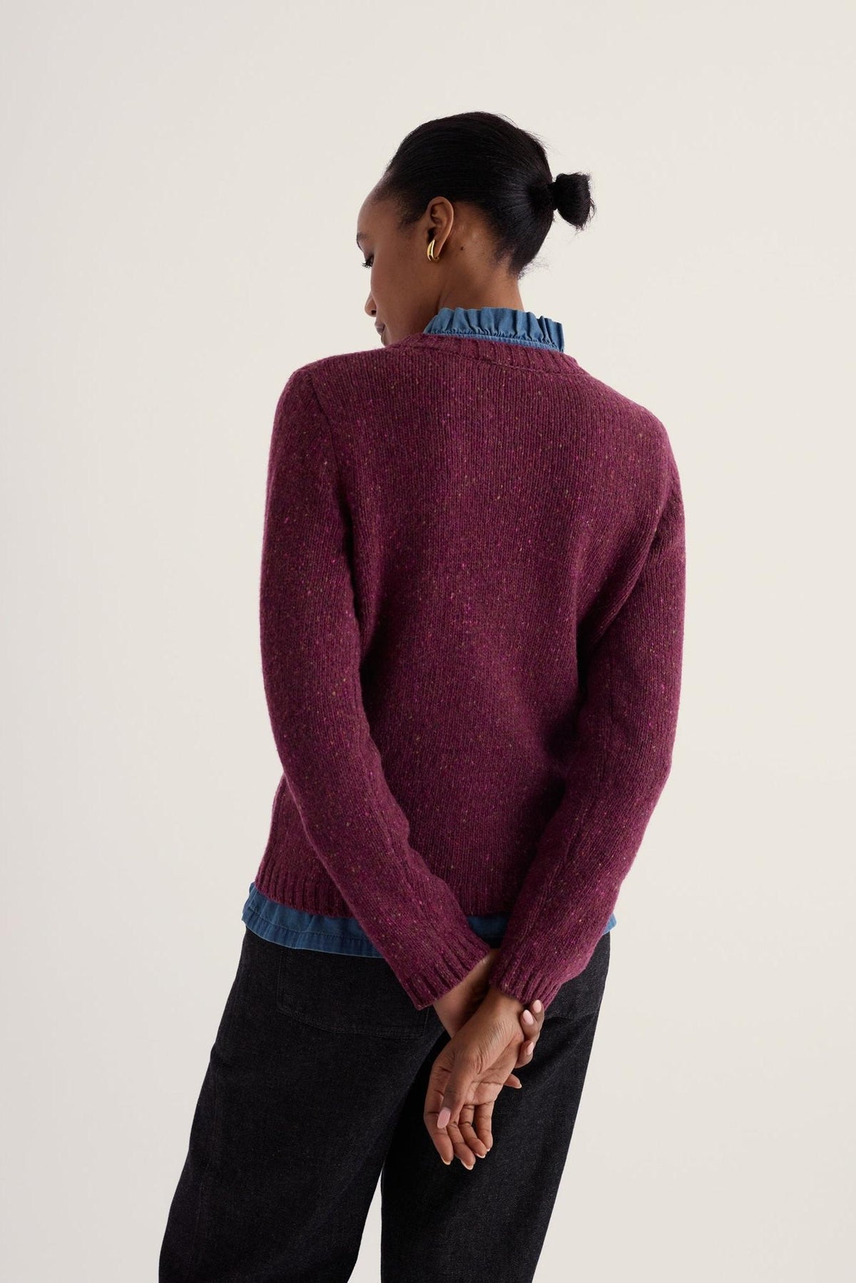Woman seen from behind wearing a textured plum merino wool jumper layered over a blue collared shirt.