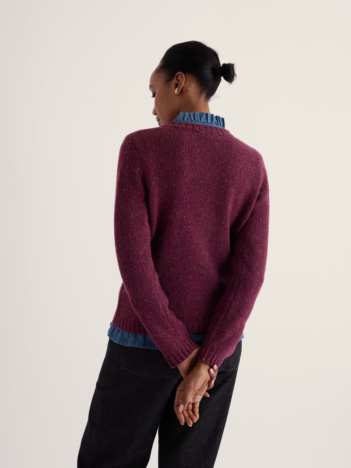 Woman seen from behind wearing a textured plum merino wool jumper layered over a blue collared shirt.