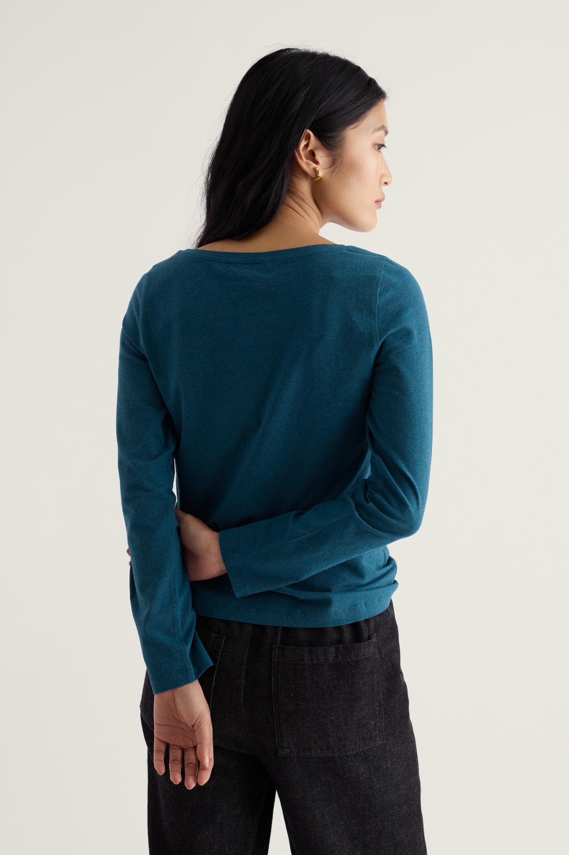 A woman wearing a long-sleeved blue Seasalt Cornwall organic cotton top, viewed from the back.