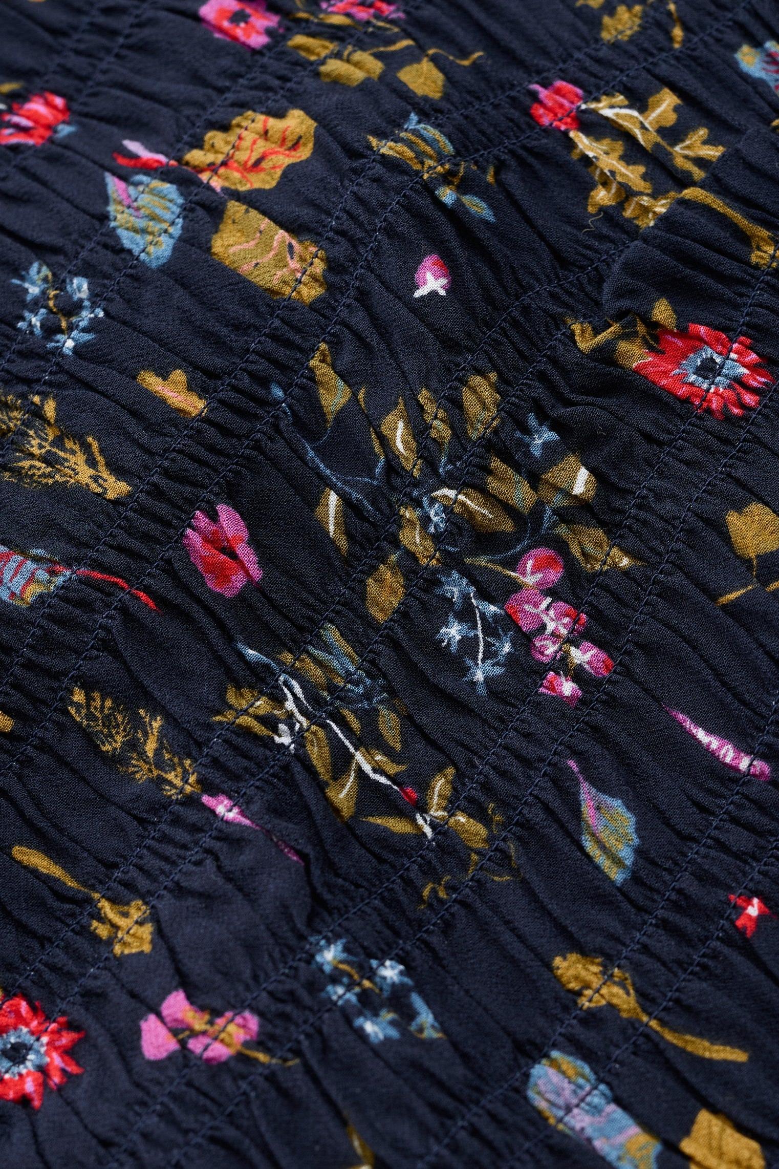 Close-up of a dark navy or black fabric with a dense multicolor floral and botanical print, featuring pink, red, yellow, and blue flowers with textured stitched details.