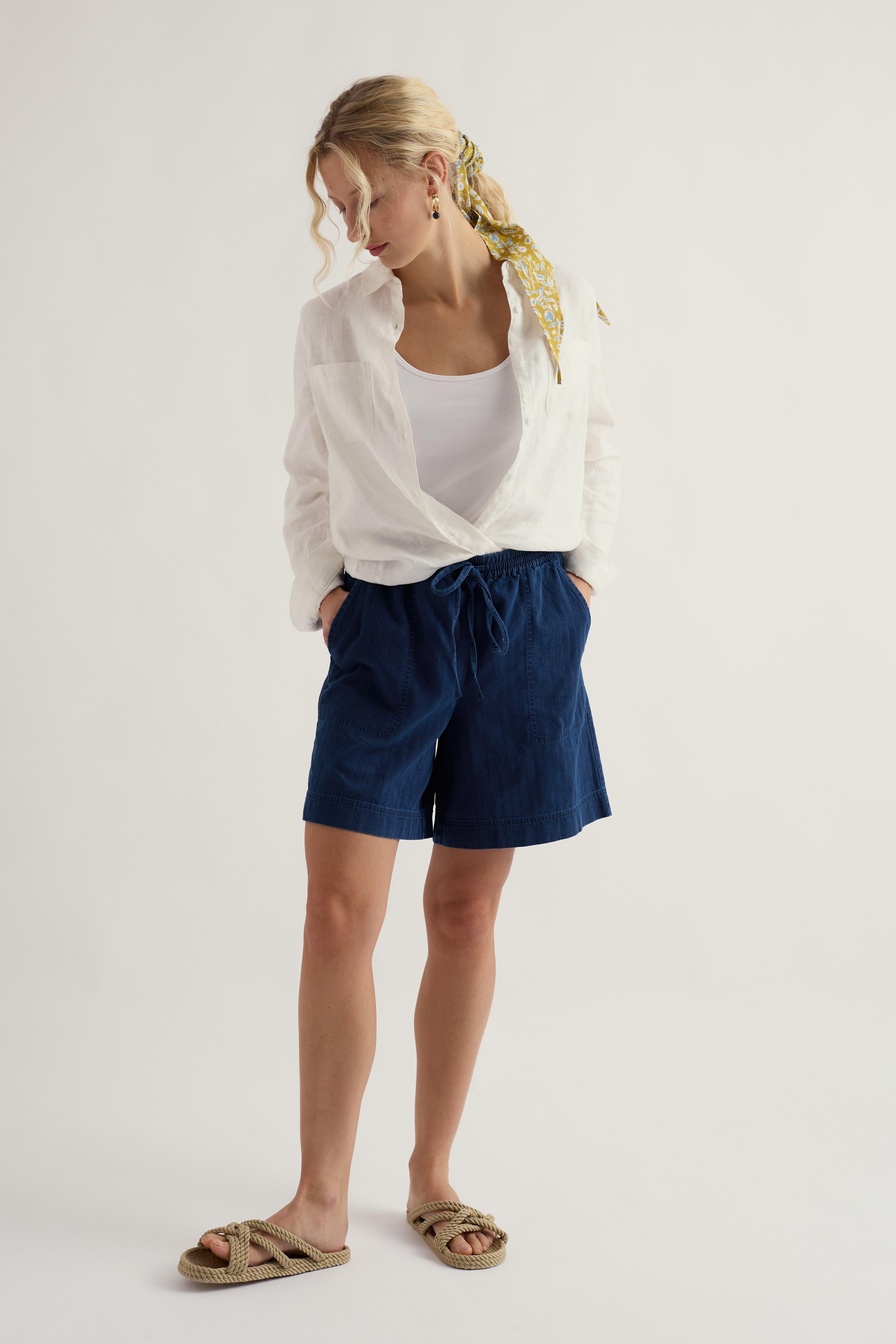 Woman wearing a white shirt, white top, and blue shorts on a light background