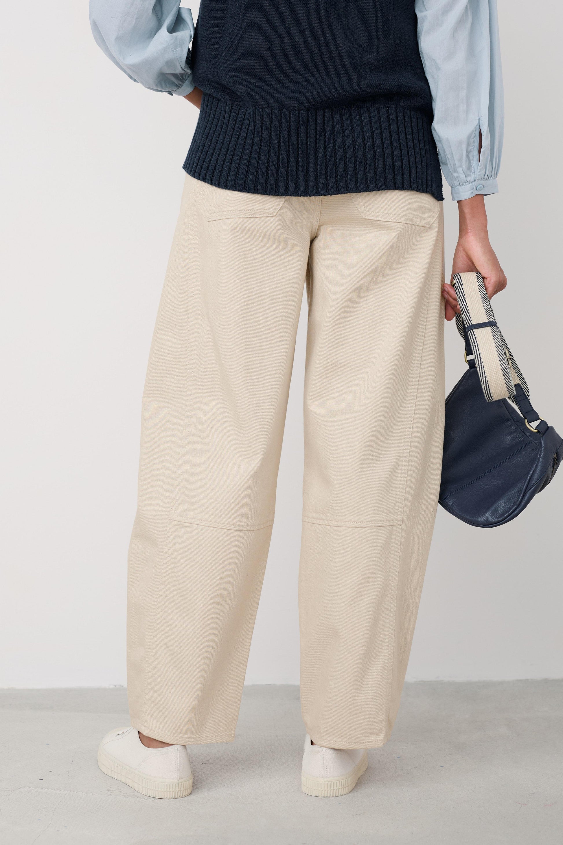 Person wearing beige wide-leg pants with a navy sweater and light blue shirt, holding a navy bag.