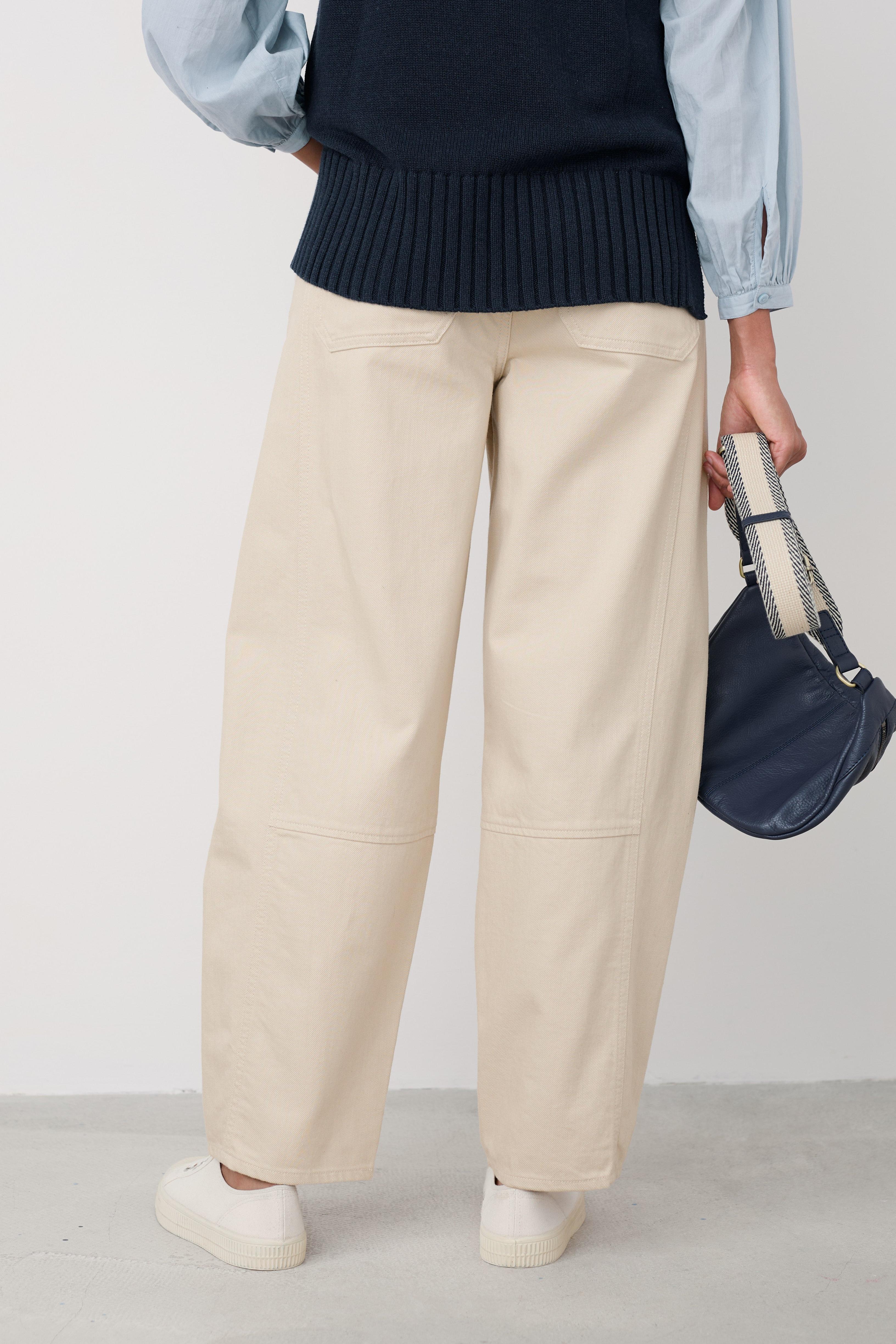 Person wearing beige wide-leg pants with a navy sweater and light blue shirt, holding a navy bag.