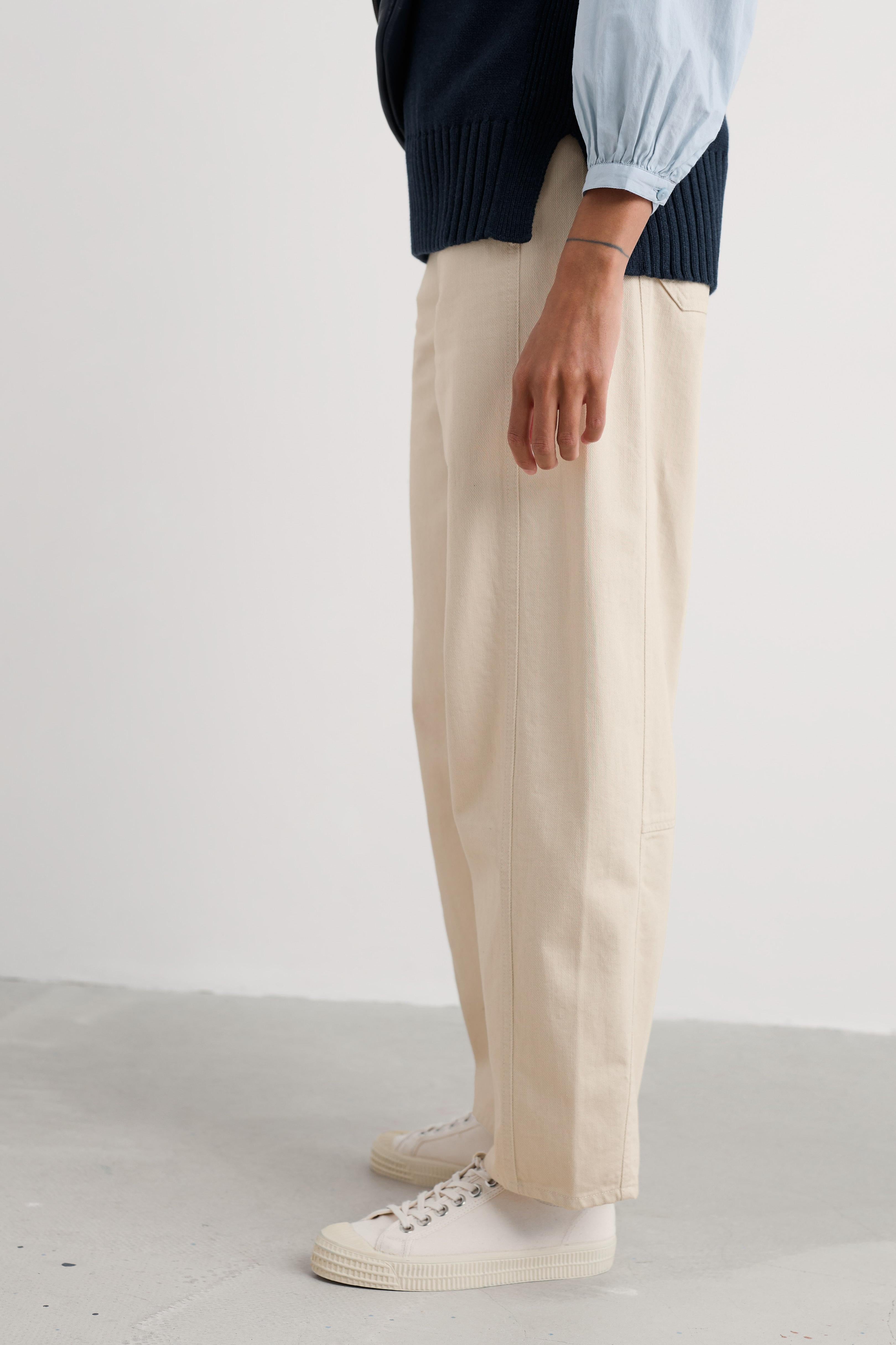 Person wearing beige organic cotton pants and white sneakers on a plain background