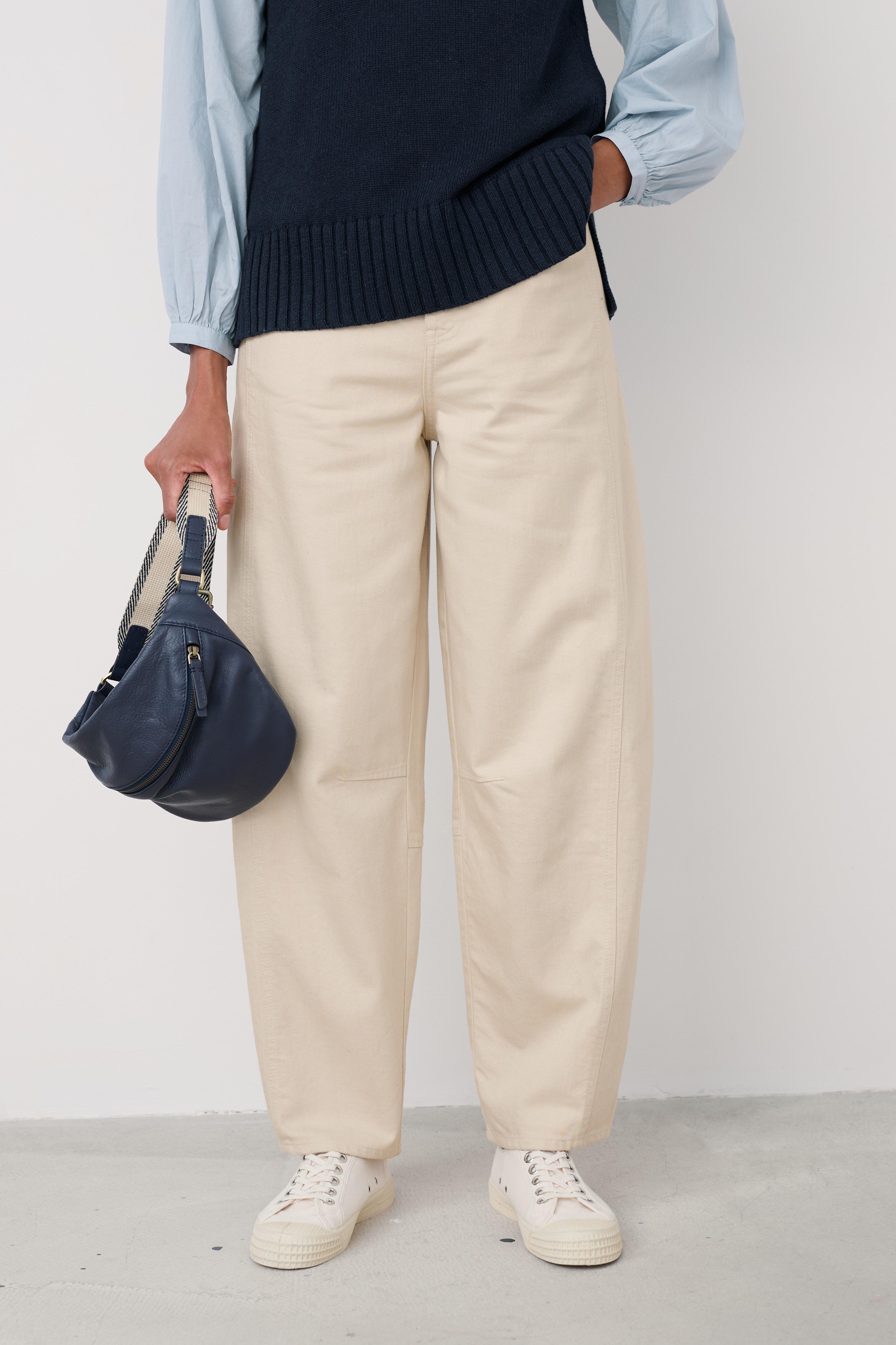 Person wearing a navy sweater vest, light blue shirt, beige pants, and white sneakers, holding a blue handbag.