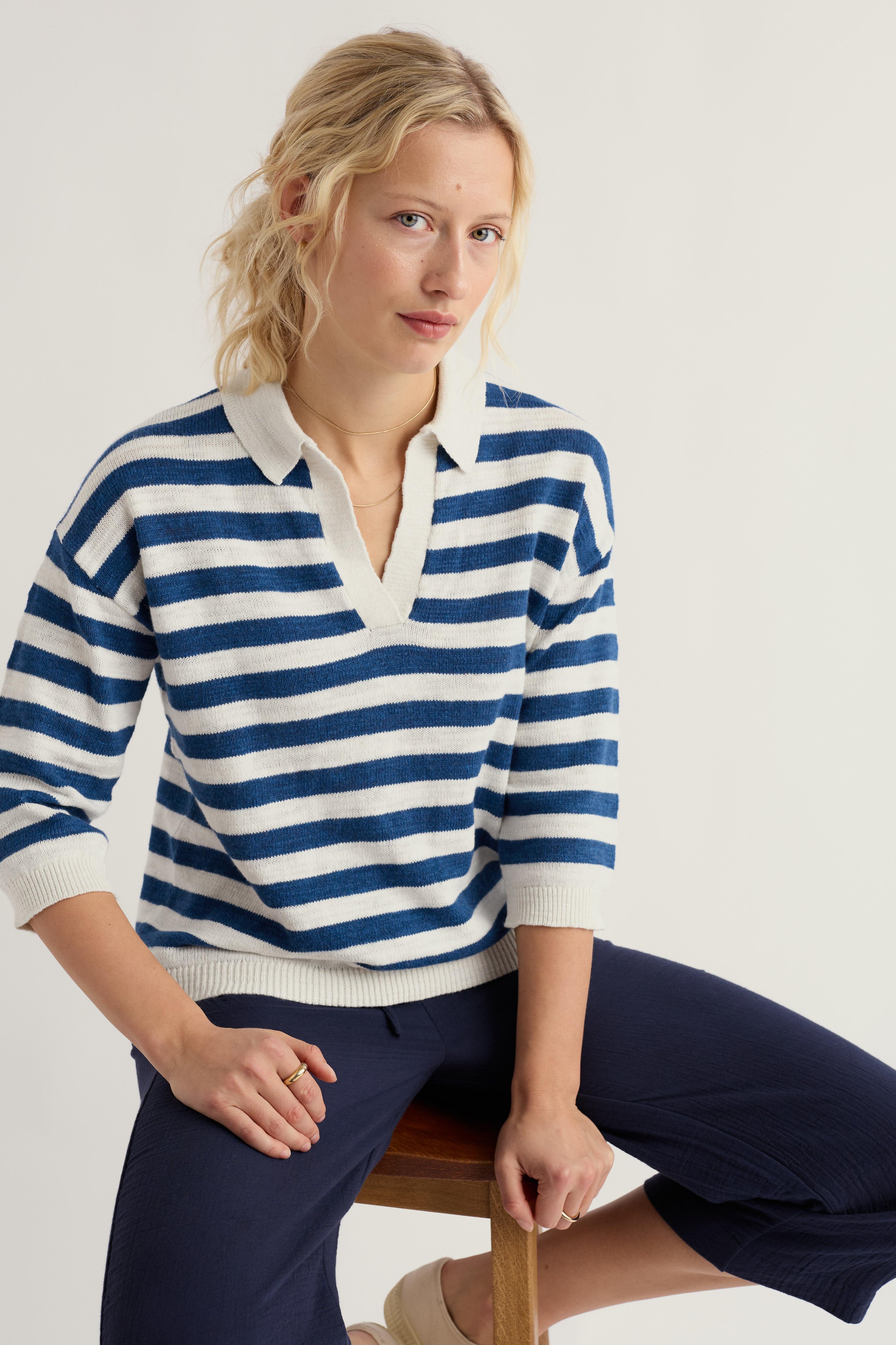 Woman wearing a blue and white striped sweater sitting on a chair against a white background