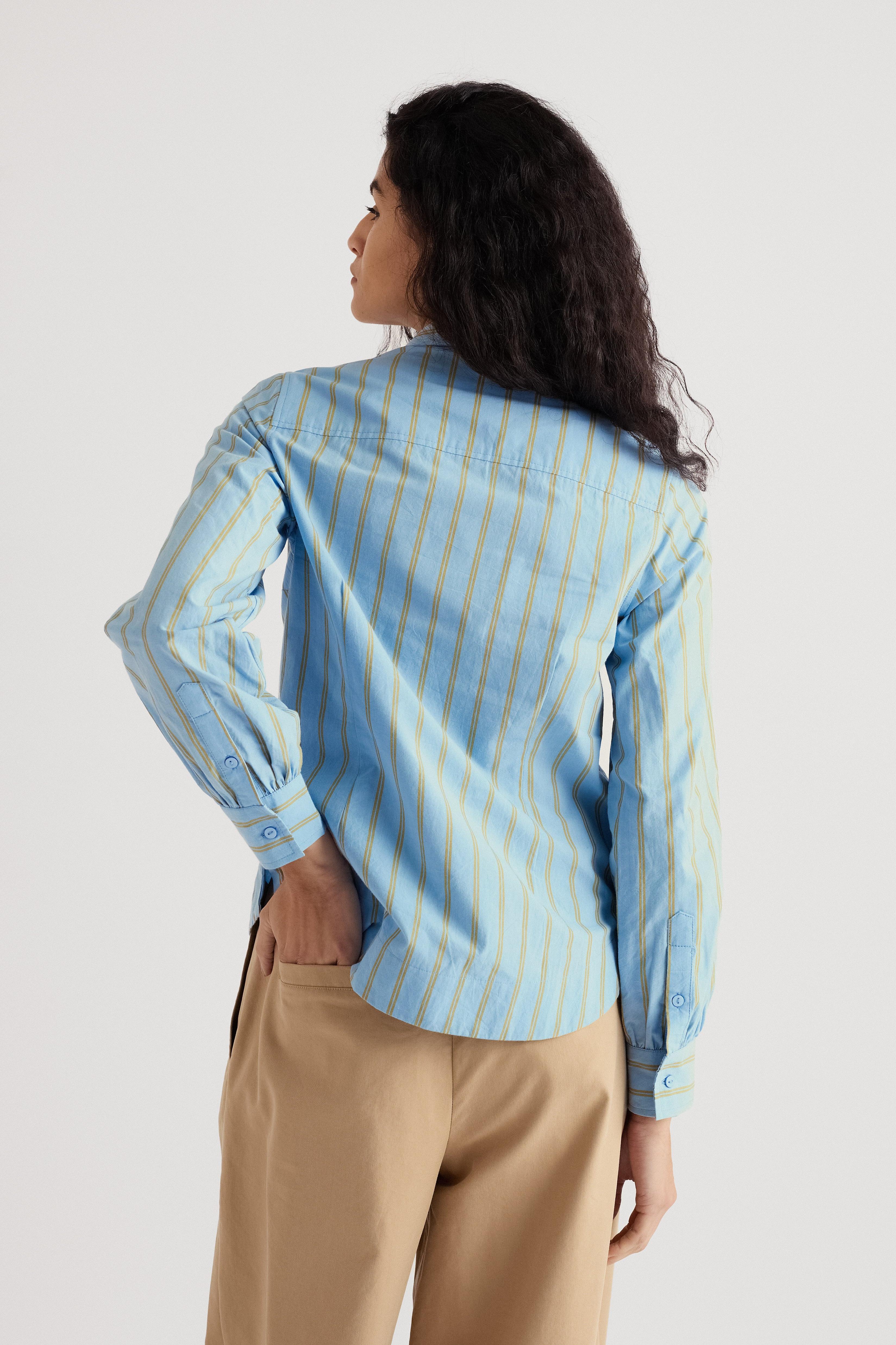 Woman wearing a blue striped shirt and beige pants on a light gray background