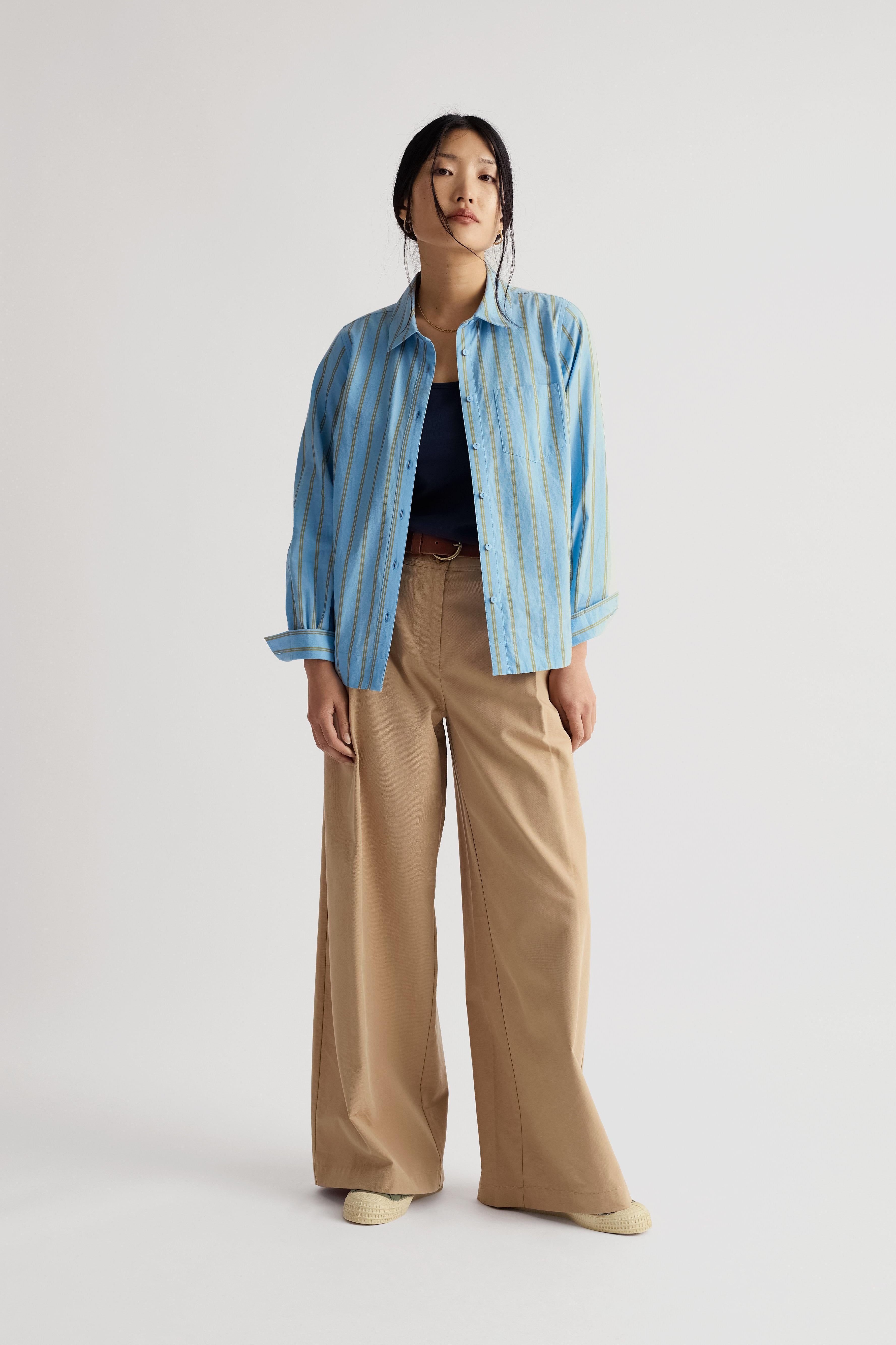 Woman wearing a blue striped shirt and beige pants on a white background