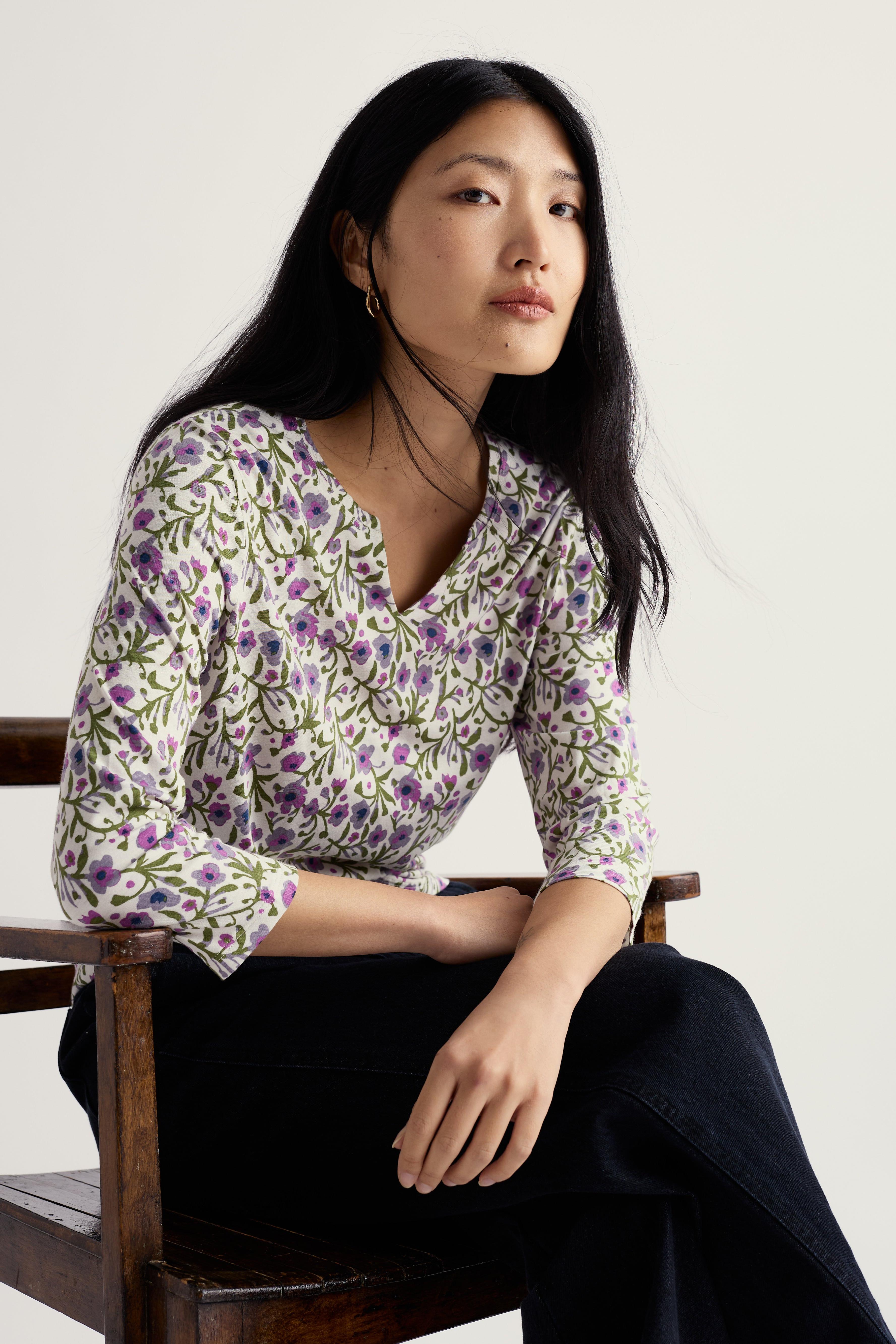 Woman wearing a floral organic cotton blouse sitting on a chair against a white background