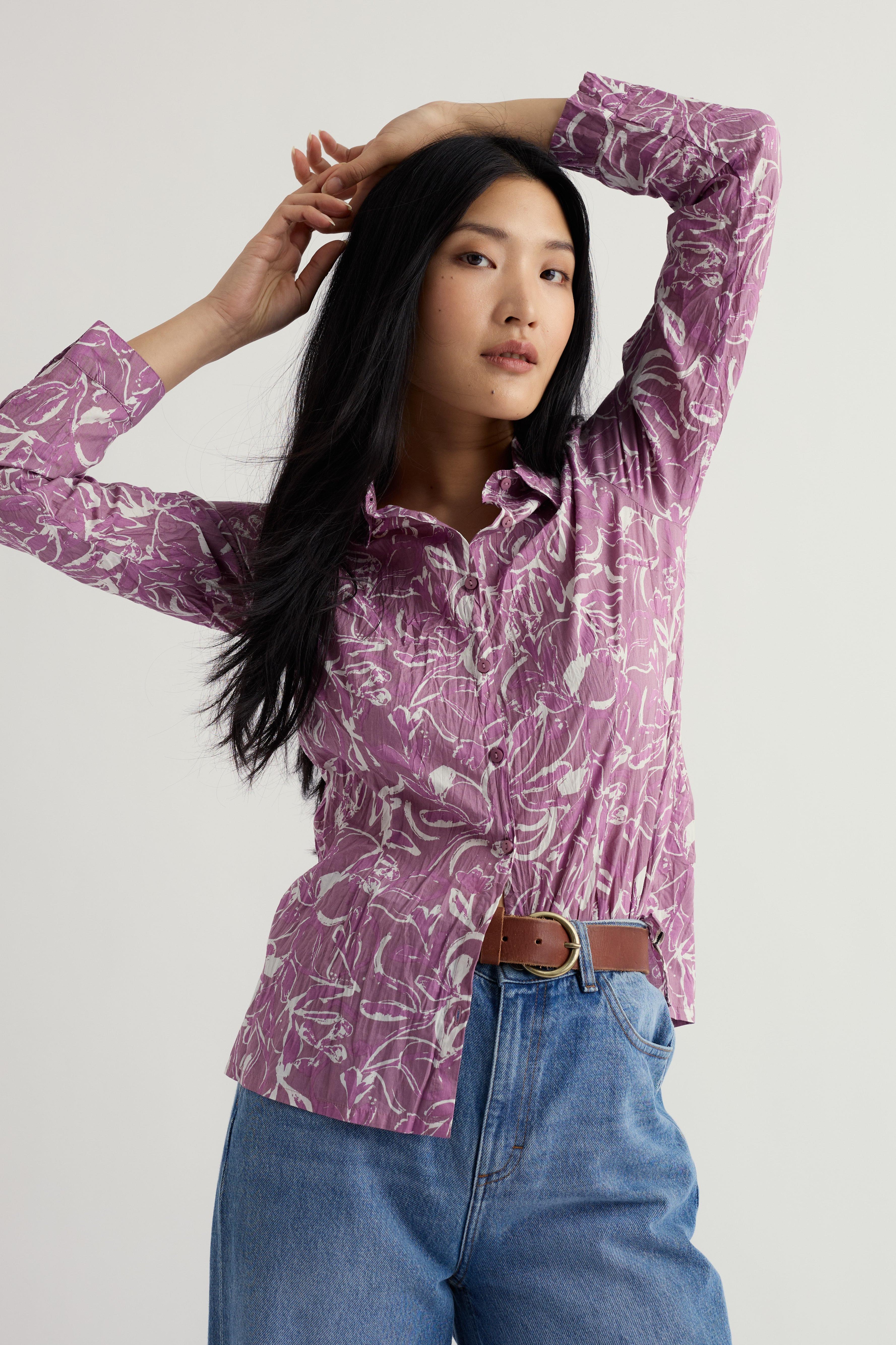 Woman wearing a purple patterned shirt and blue jeans on a plain background