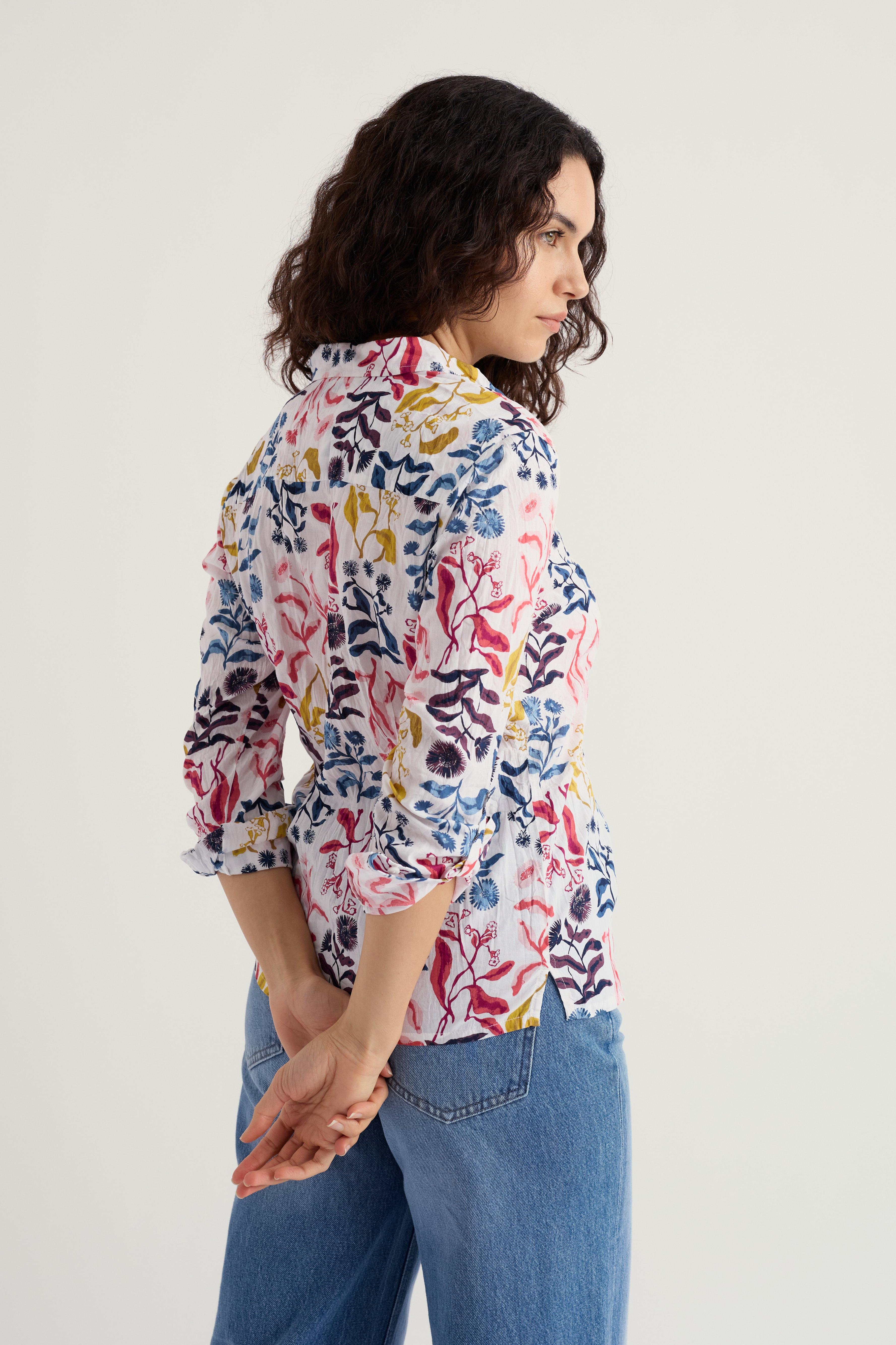 Woman wearing a floral organic cotton shirt and blue jeans against a plain background