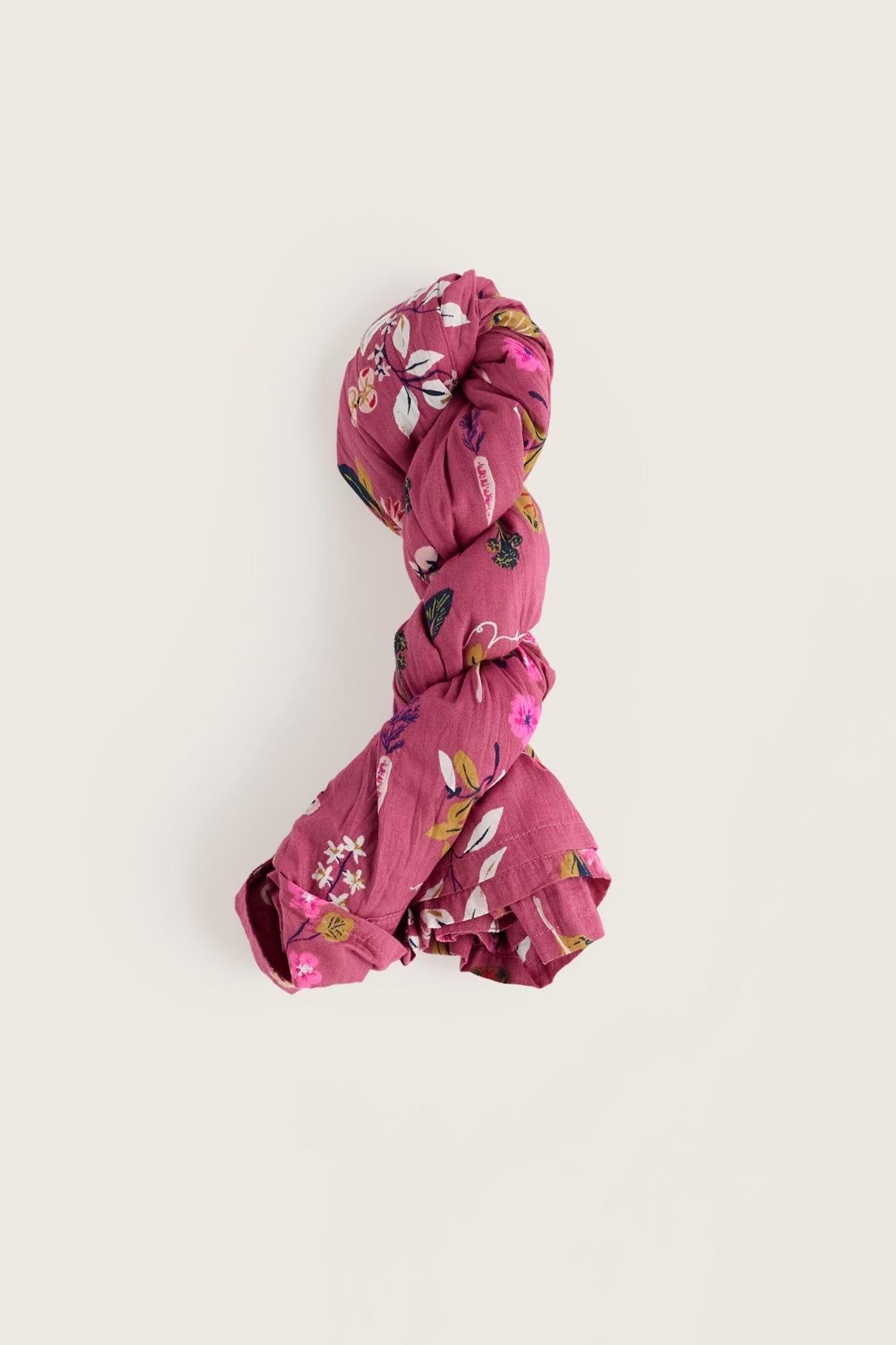A knotted pink shirt with a white, green, and yellow floral print, displayed on a solid light beige background.