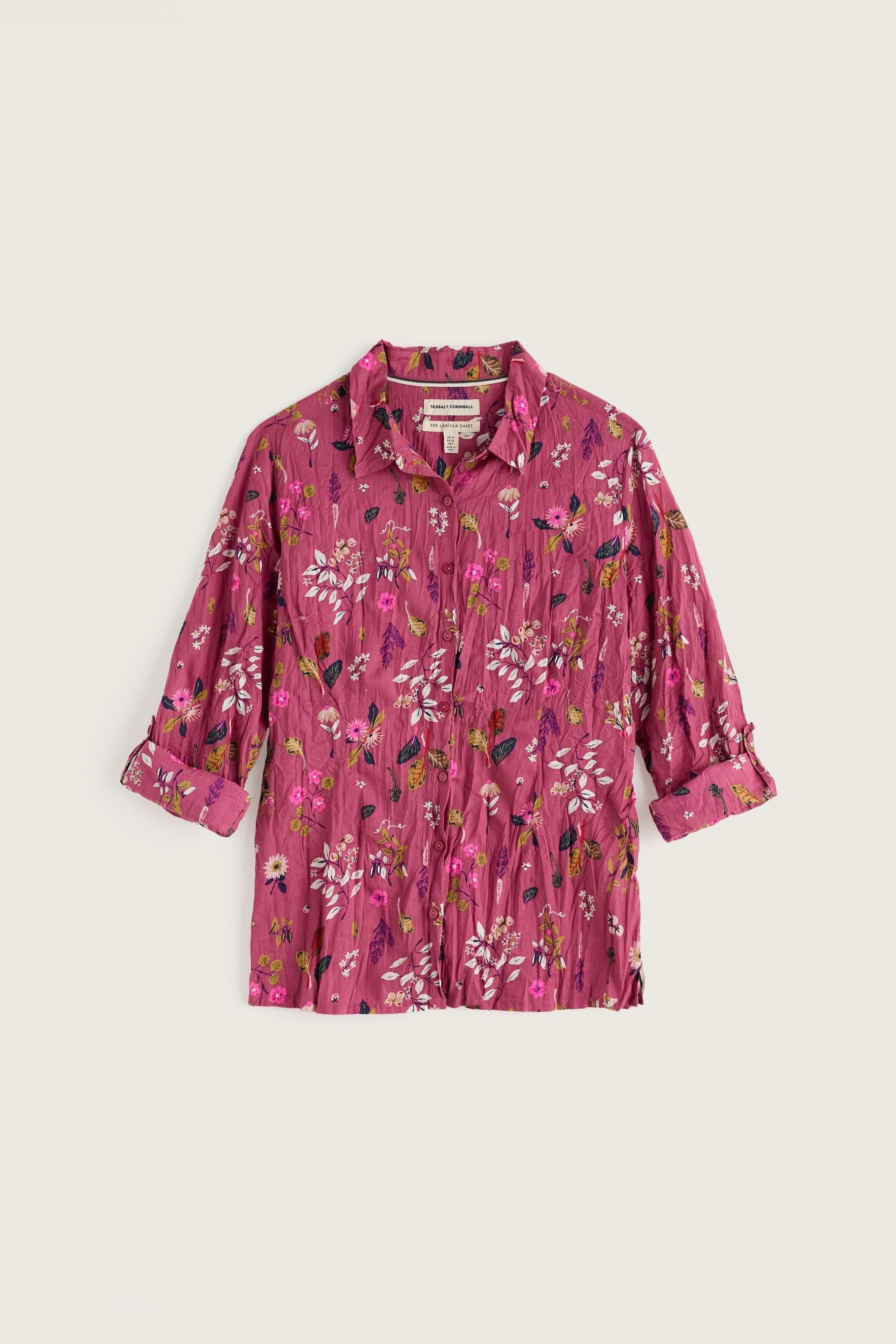 A pink long-sleeve button-up shirt with a dense multicolor floral and bird print, laid flat against a light beige background.