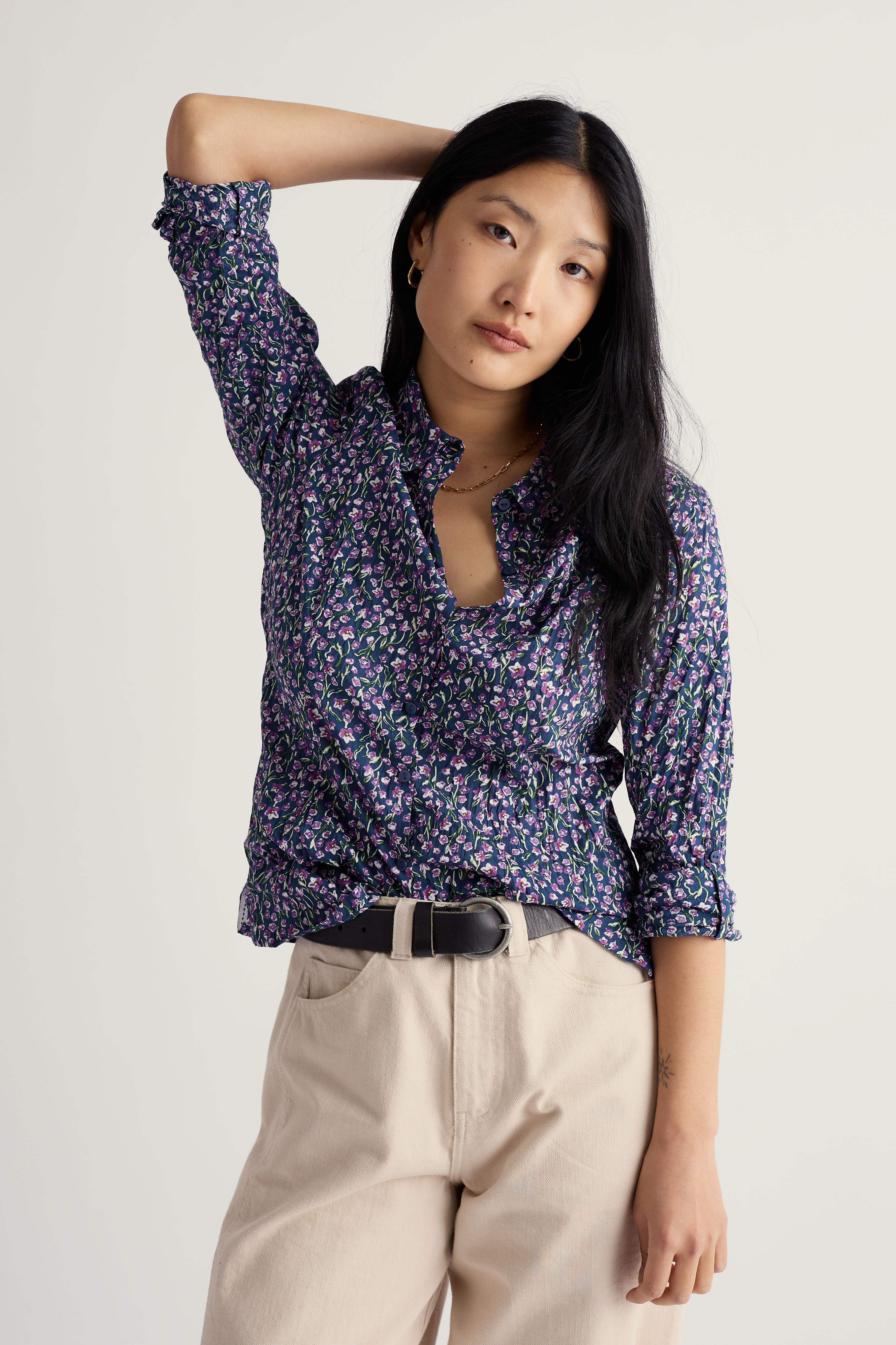 Woman wearing a floral organic cotton blouse and beige pants on a plain background