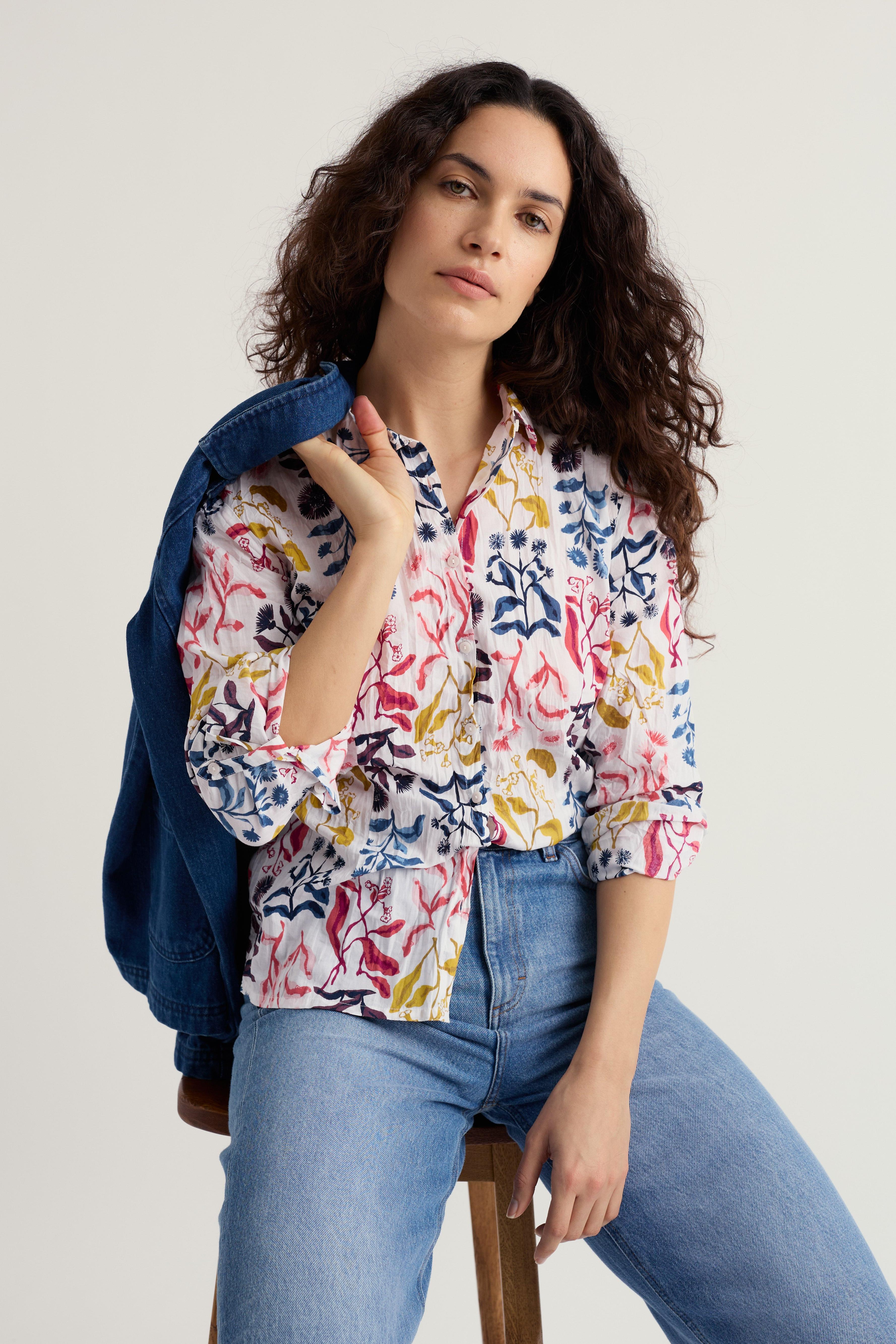 Woman wearing a colorful floral blouse and blue jeans, holding a denim jacket.