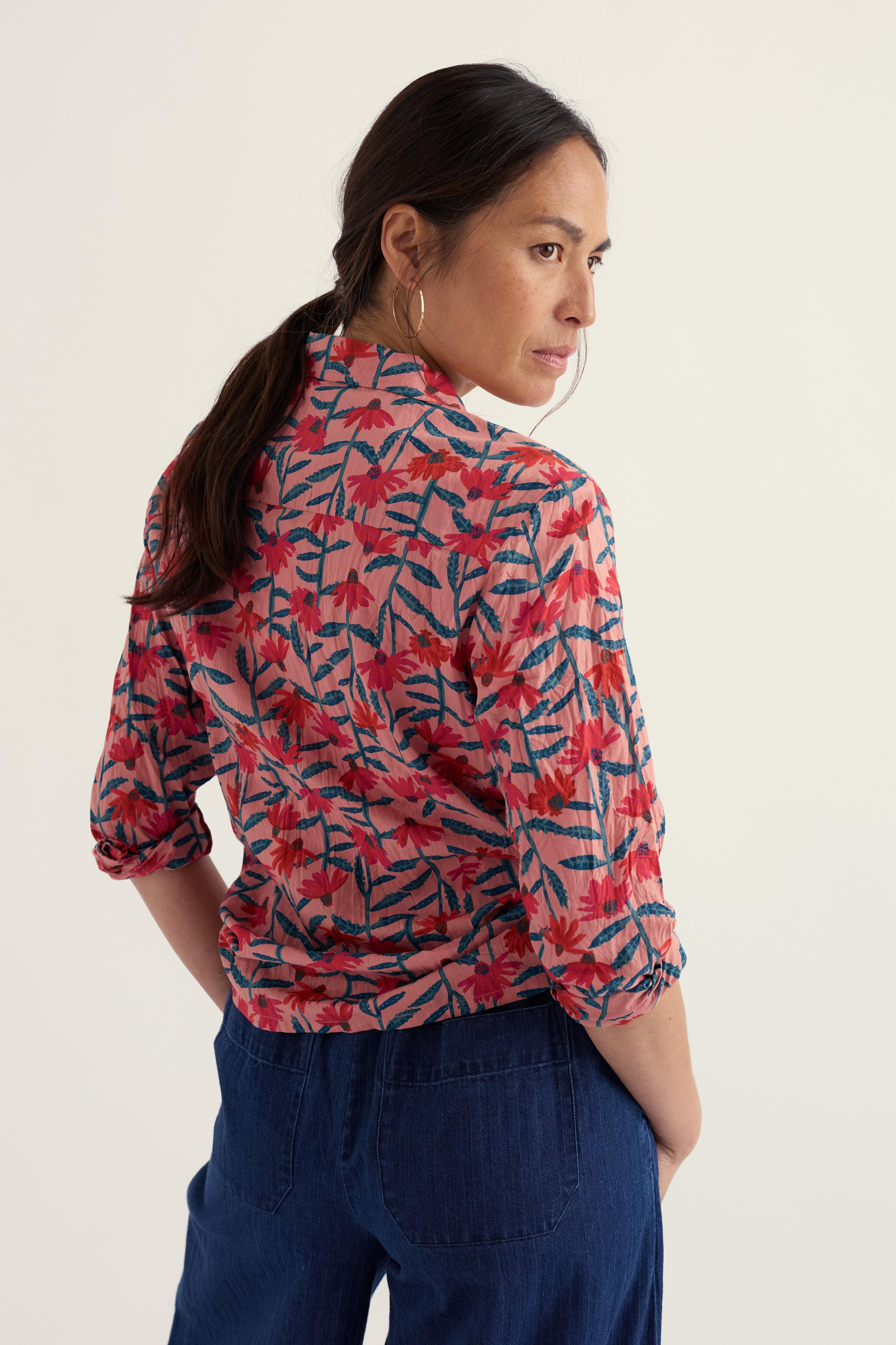 Woman wearing a red and blue patterned shirt with blue pants on a plain background