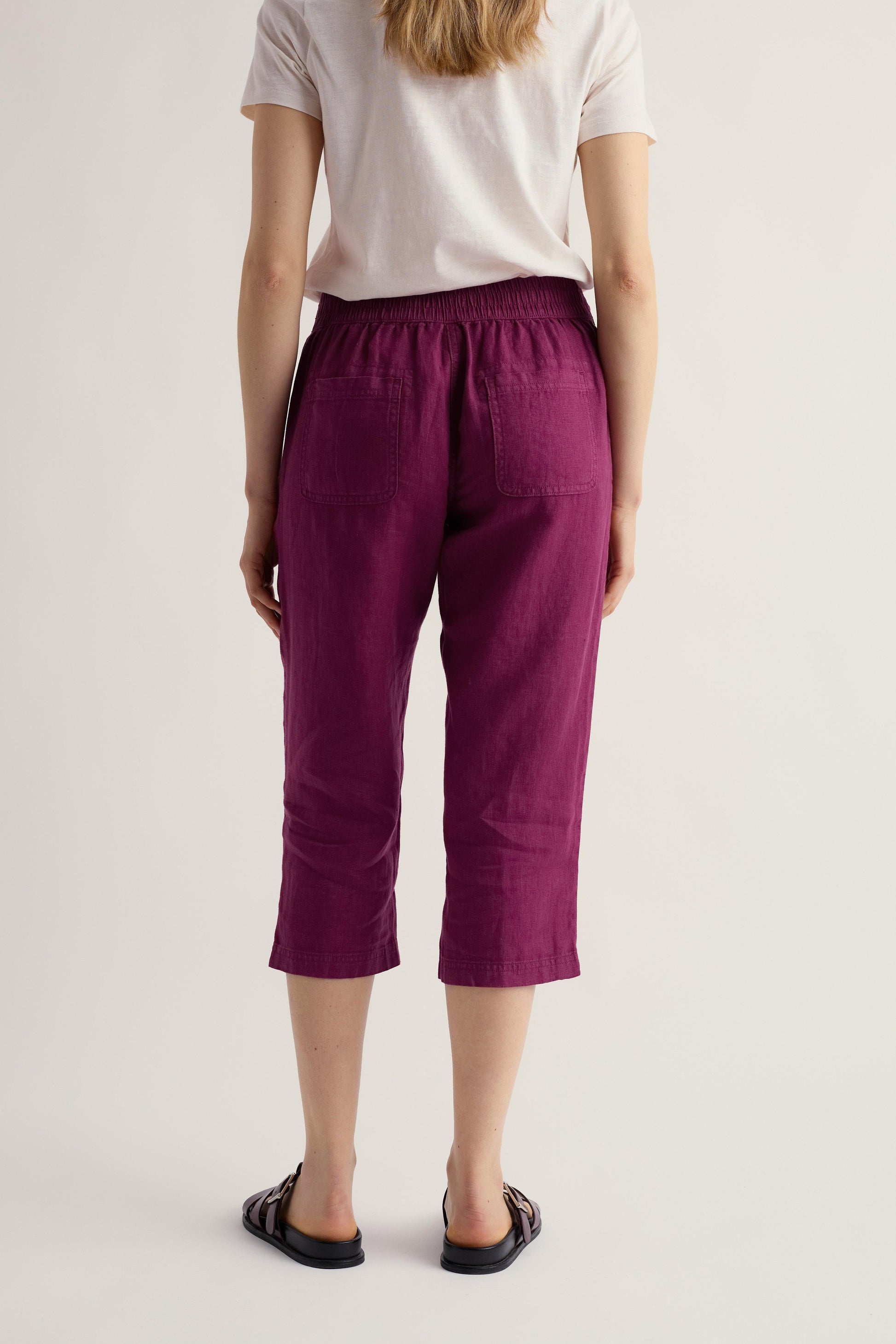 Person wearing purple cropped pants and a white shirt on a plain background