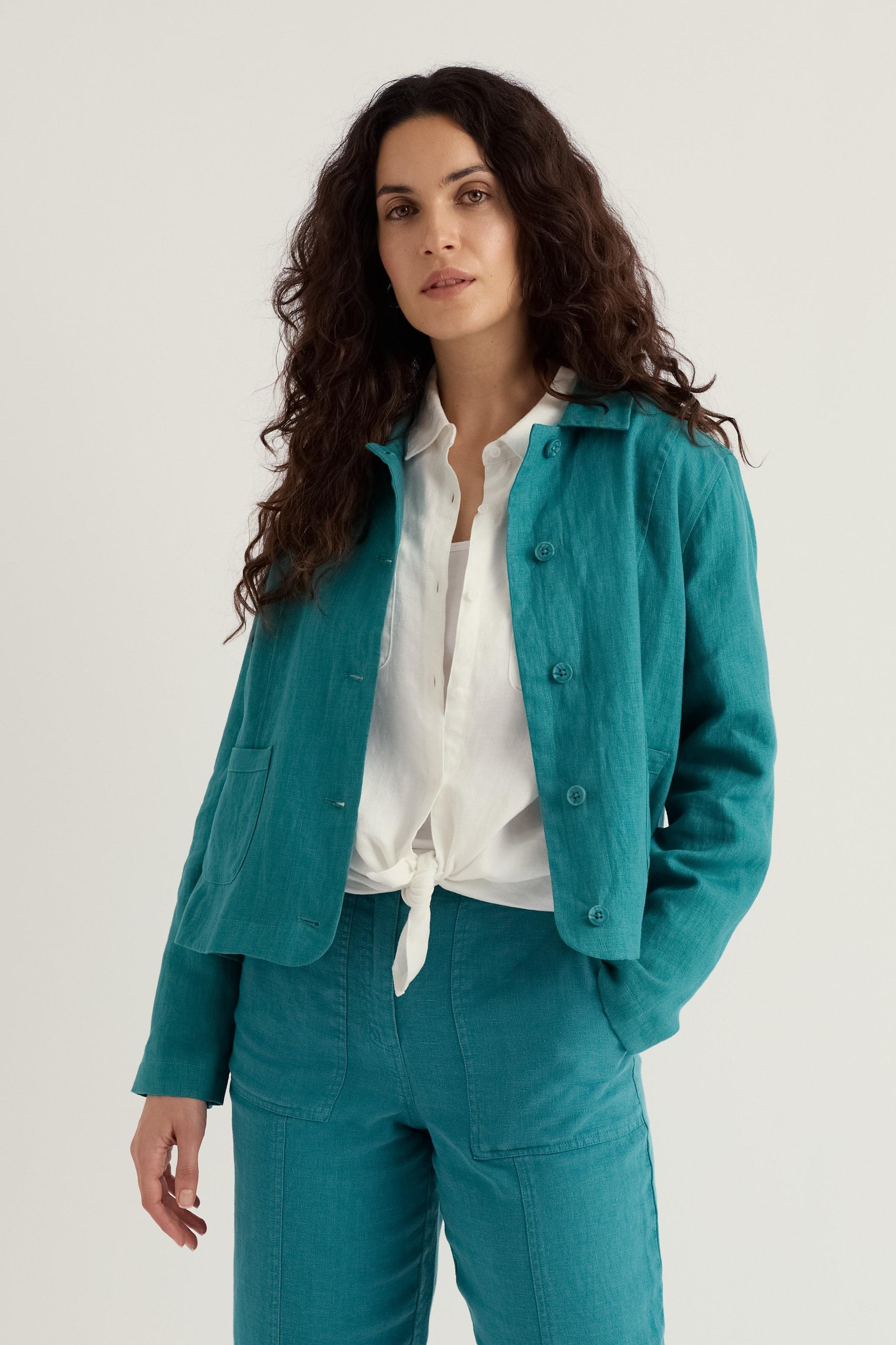 Woman wearing a teal linen jacket and pants with a white shirt on a light background