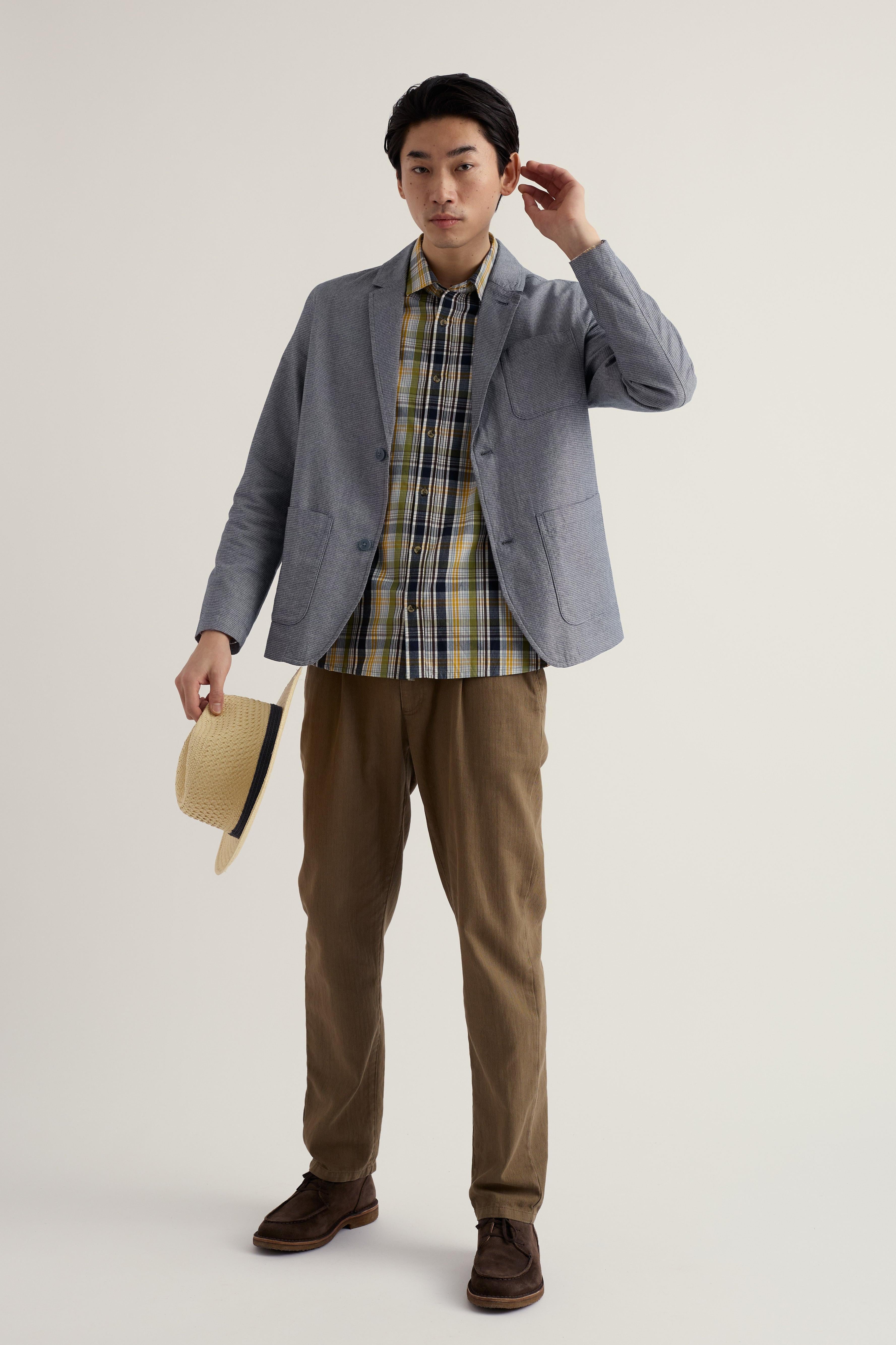 Man wearing a gray organic cotton blazer, plaid shirt, and brown pants on a light background