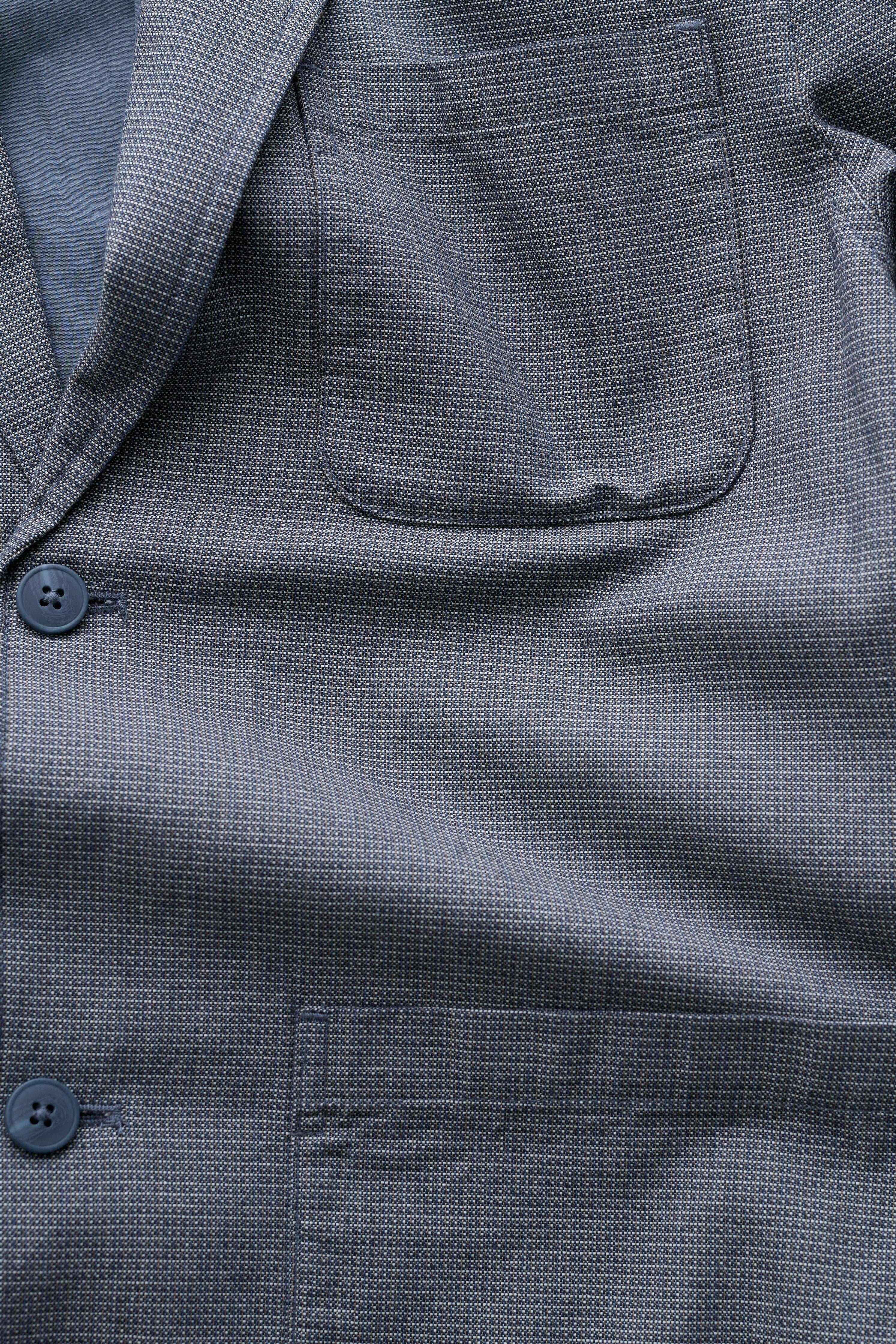 Close-up of a textured gray jacket with buttons and a pocket.