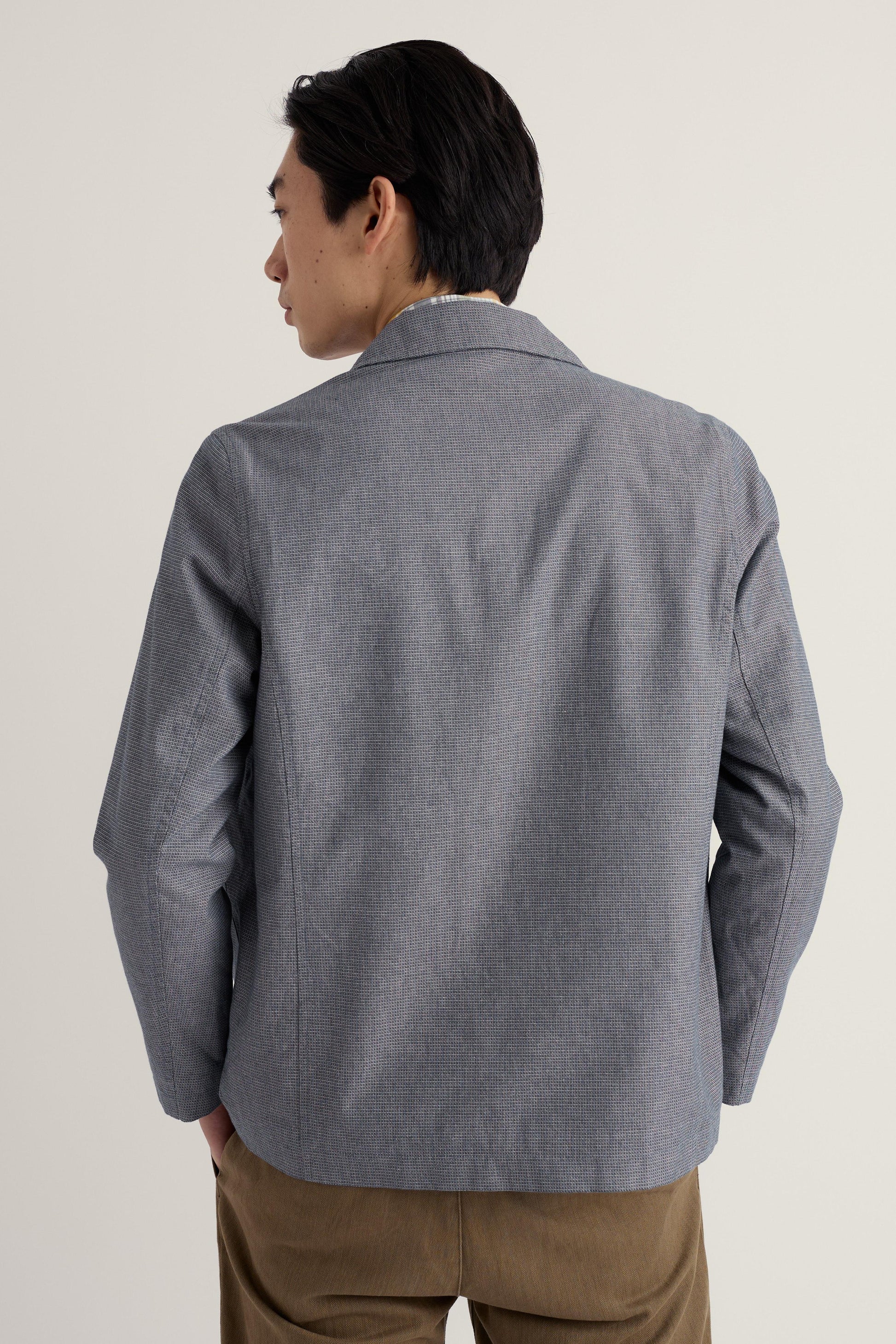 Man wearing a gray organic cotton jacket and brown pants on a plain background