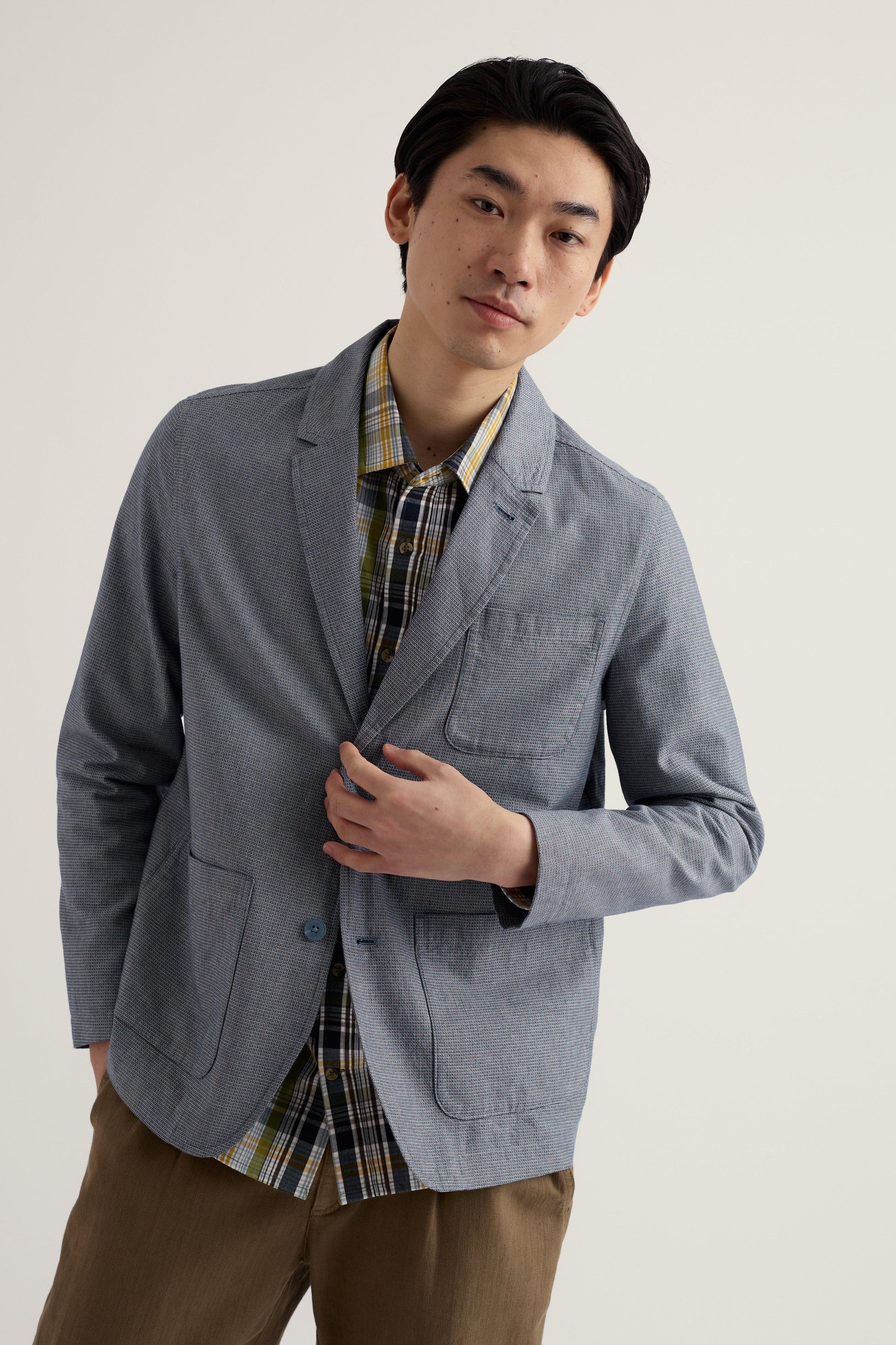 Man wearing a gray blazer over a plaid shirt with a plain background
