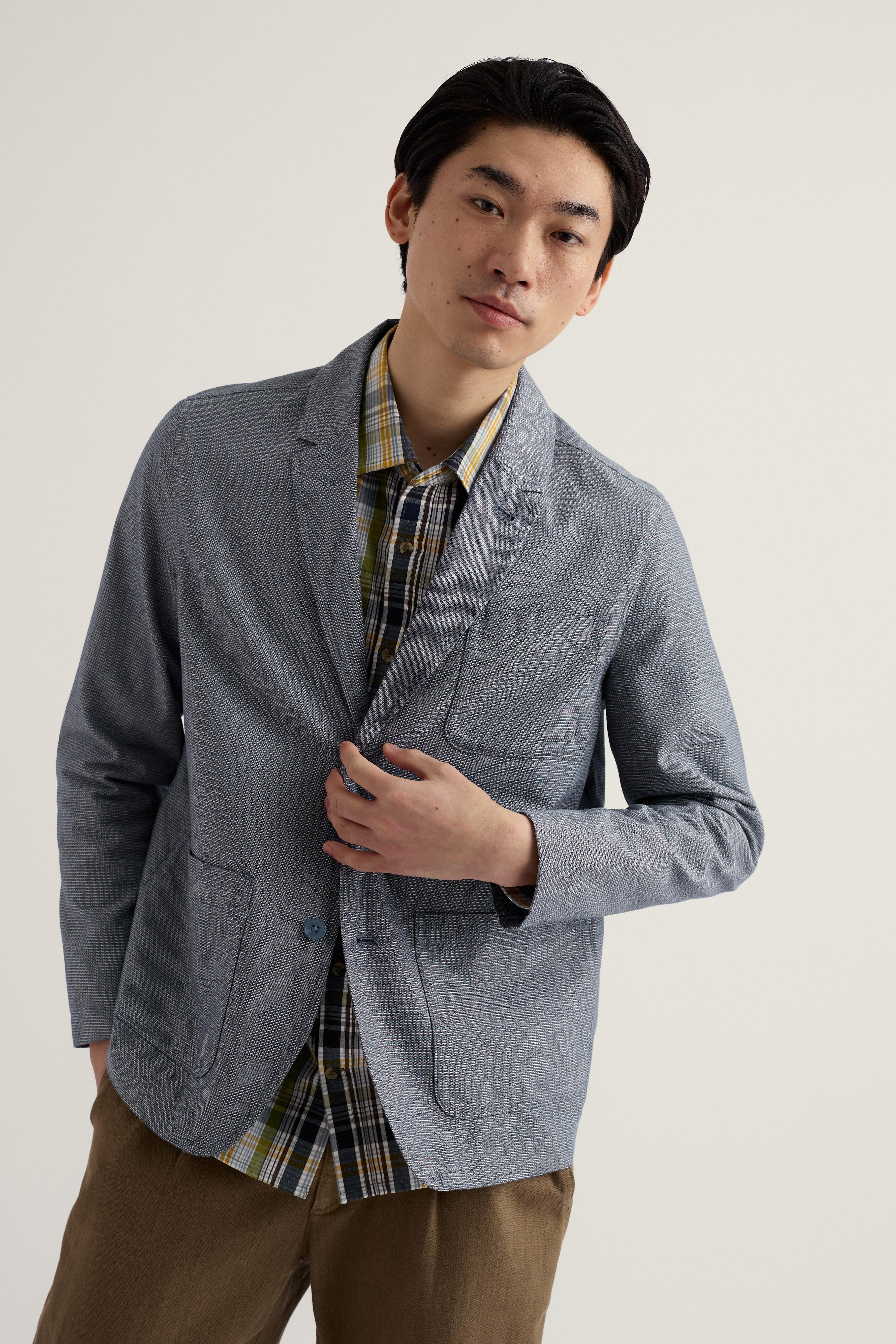 Man wearing a gray blazer over a plaid shirt with a plain background