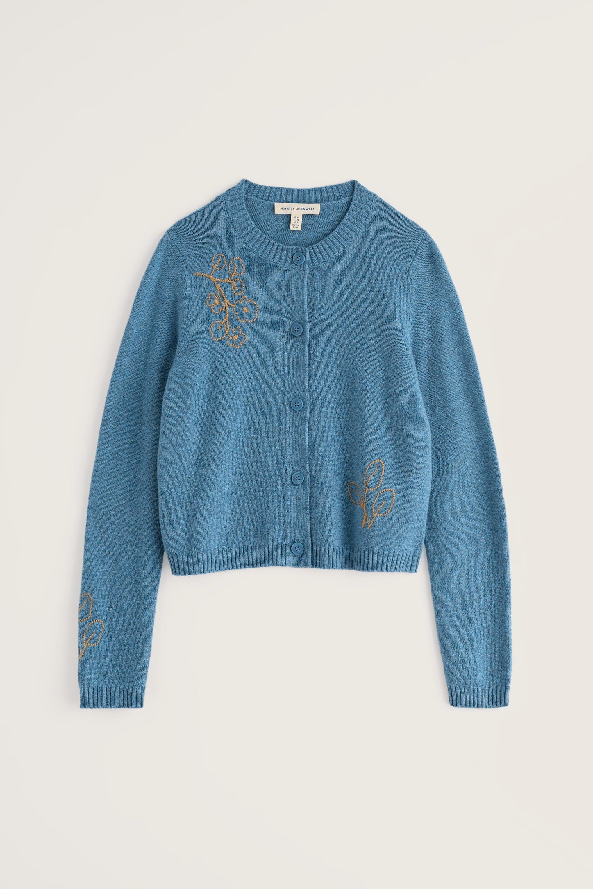 A cropped blue knit cardigan sweater with gold embroidered floral motifs on the chest and sleeves, displayed flat against a light beige background.