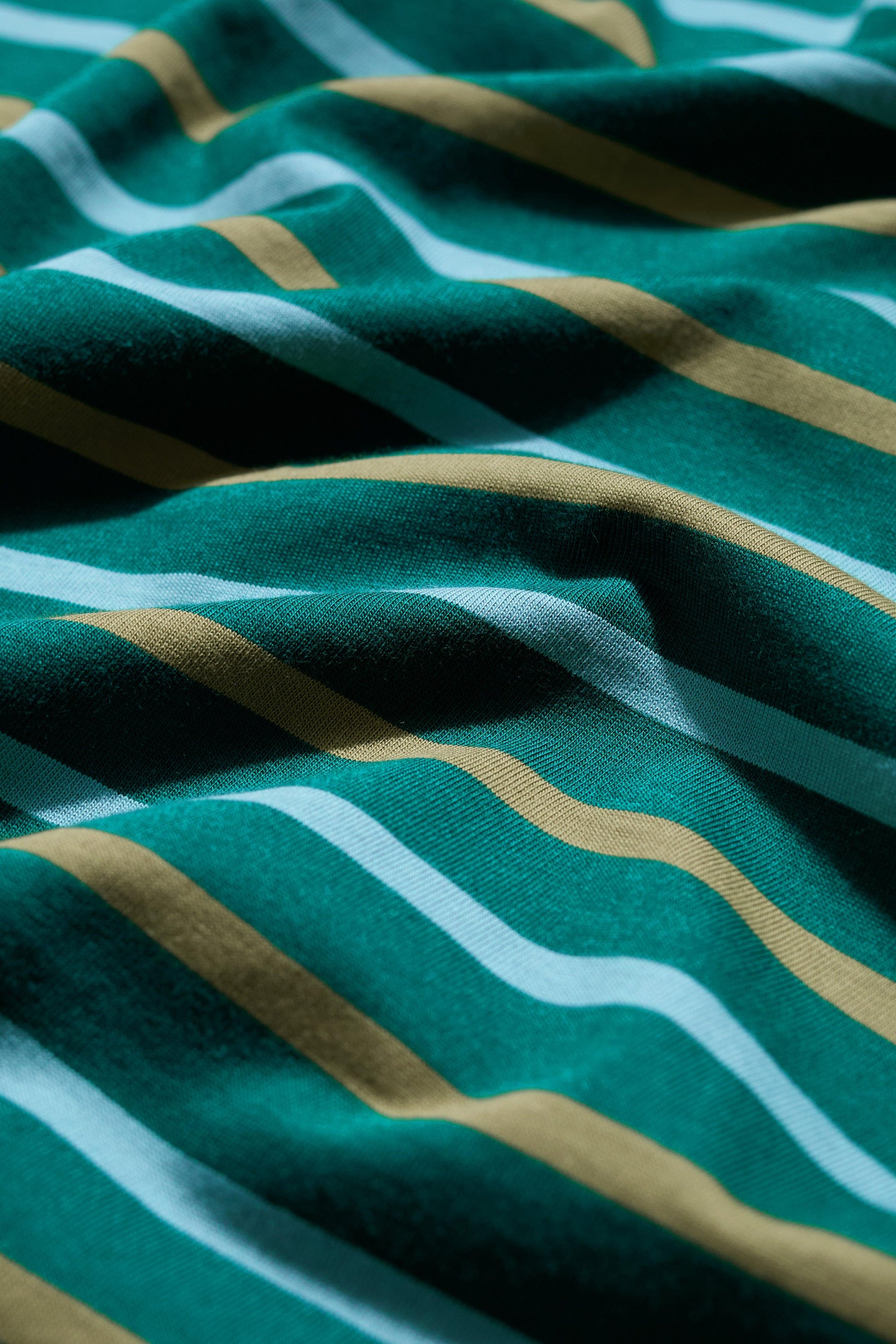 Close-up of organic cotton fabric with green, gold, and white striped pattern