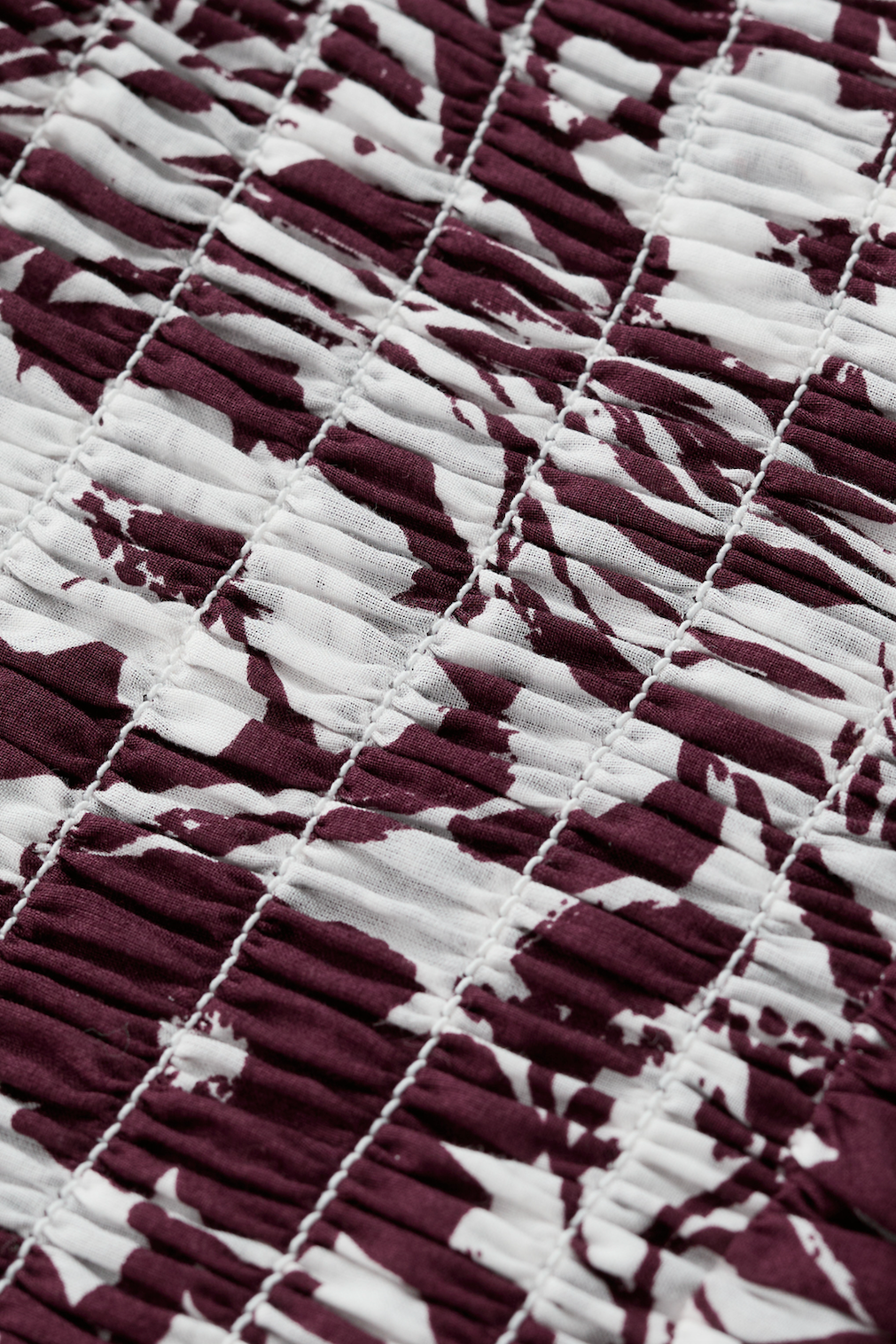Close up of burgundy and white floral organic cotton fabric with smocked texture by Seasalt.