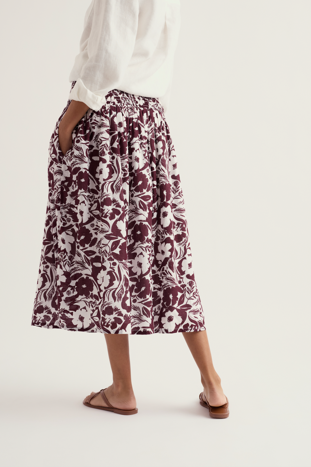 Woman wearing a floral print Seasalt organic cotton midi skirt with white linen shirt and sandals.