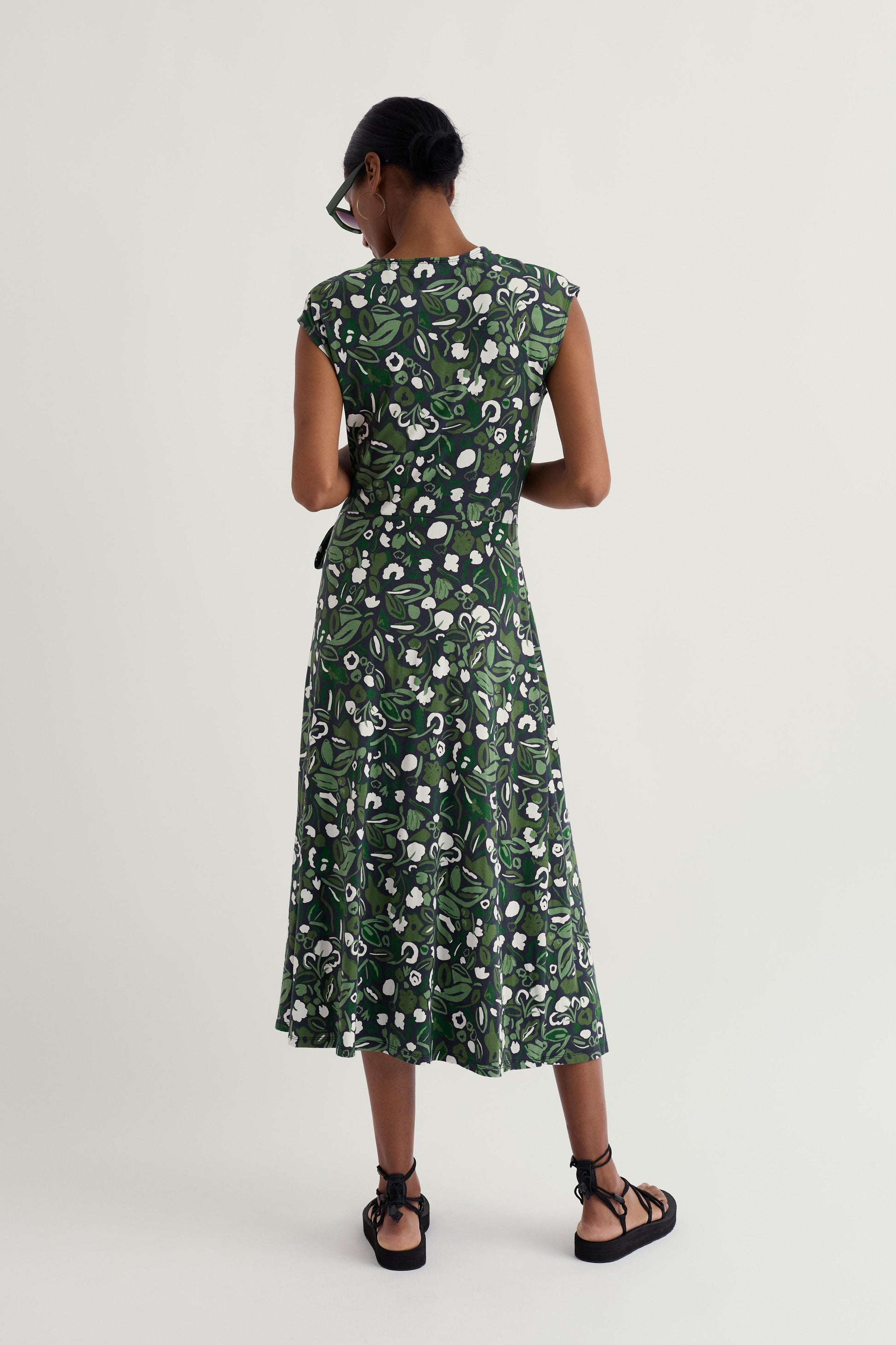 Model wearing a green floral organic cotton dress on a white background