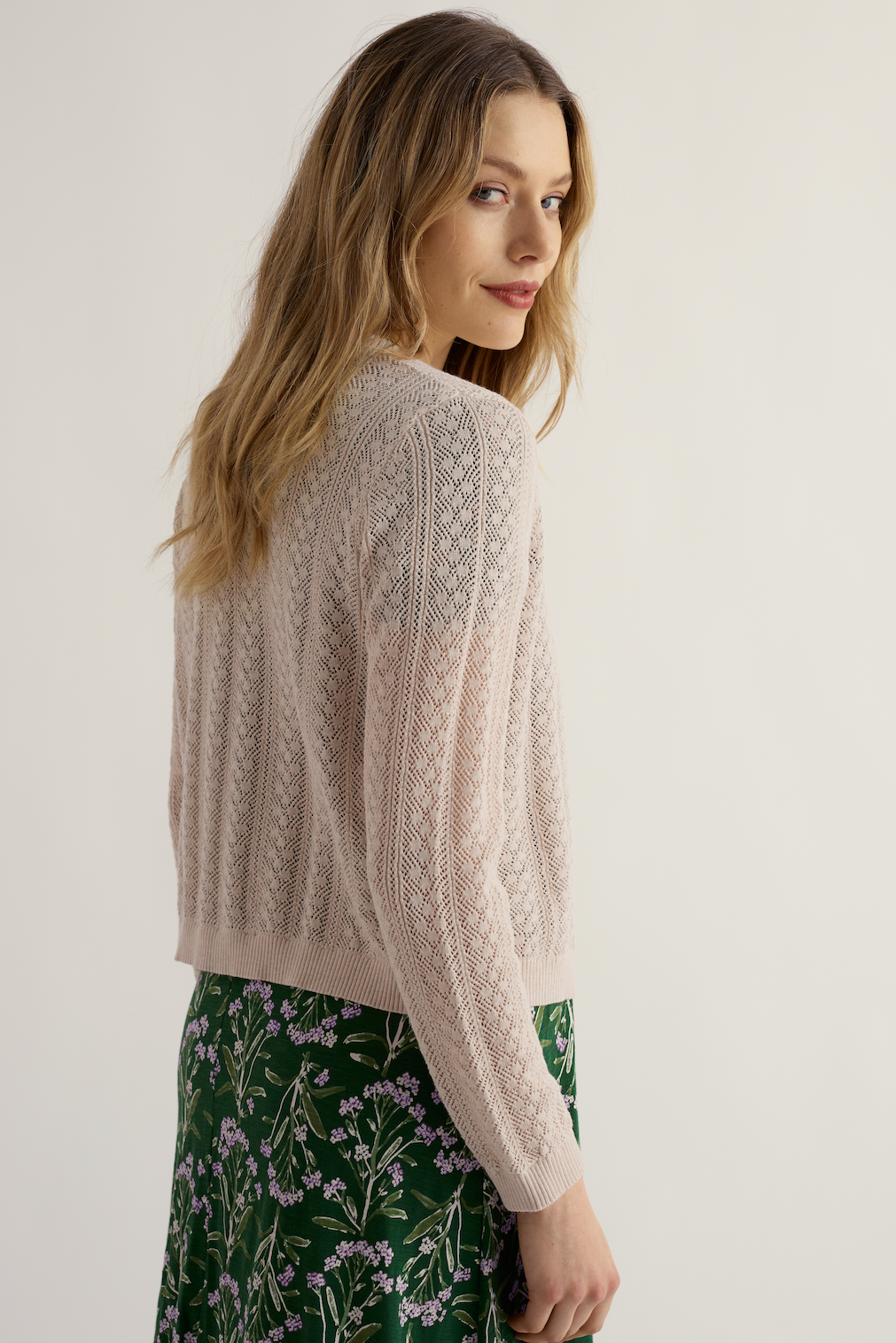 A woman wearing a Seasalt organic cotton textured sweater over a green floral skirt looking back over her shoulder.