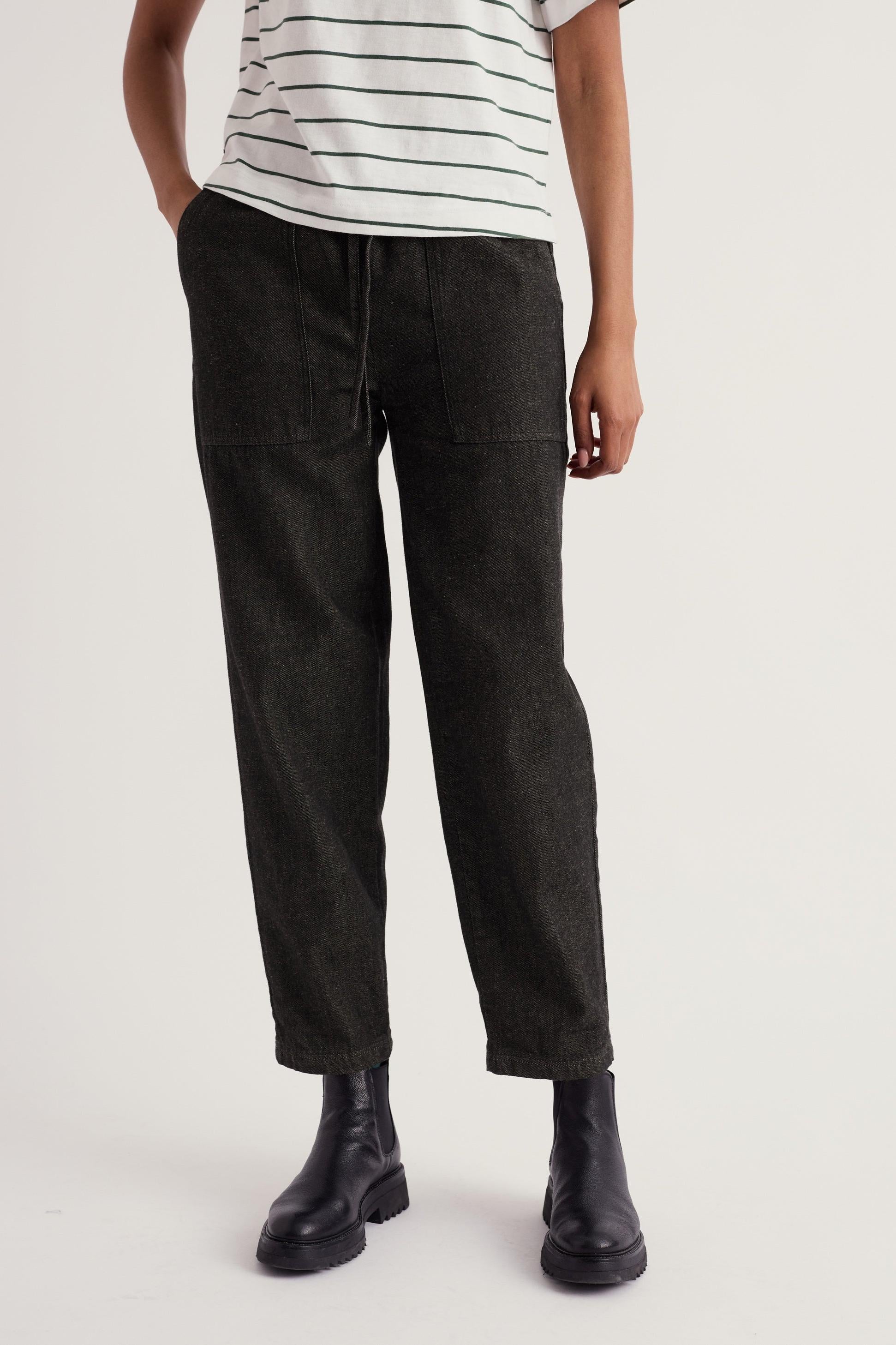 A person wearing Seasalt black organic cotton trousers and a striped top with black boots.