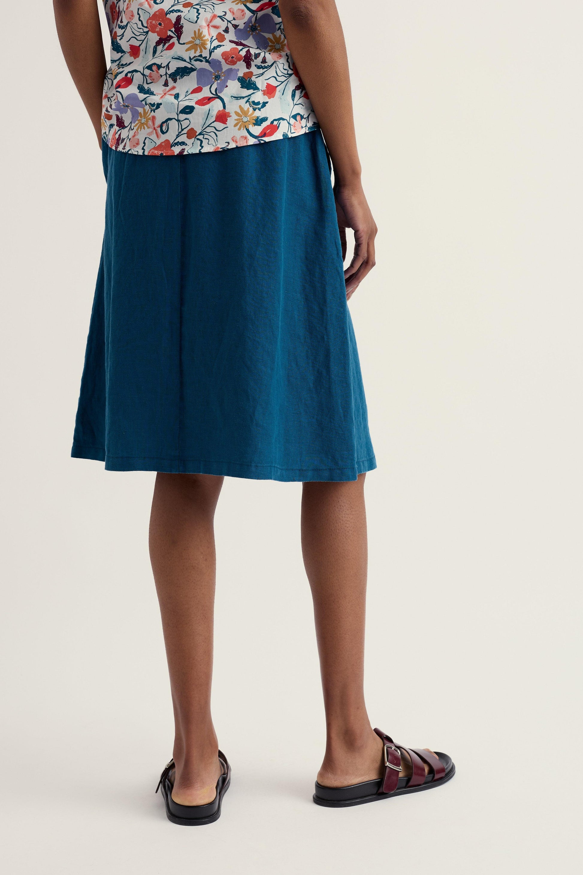 Person wearing a blue skirt and floral top on a plain background