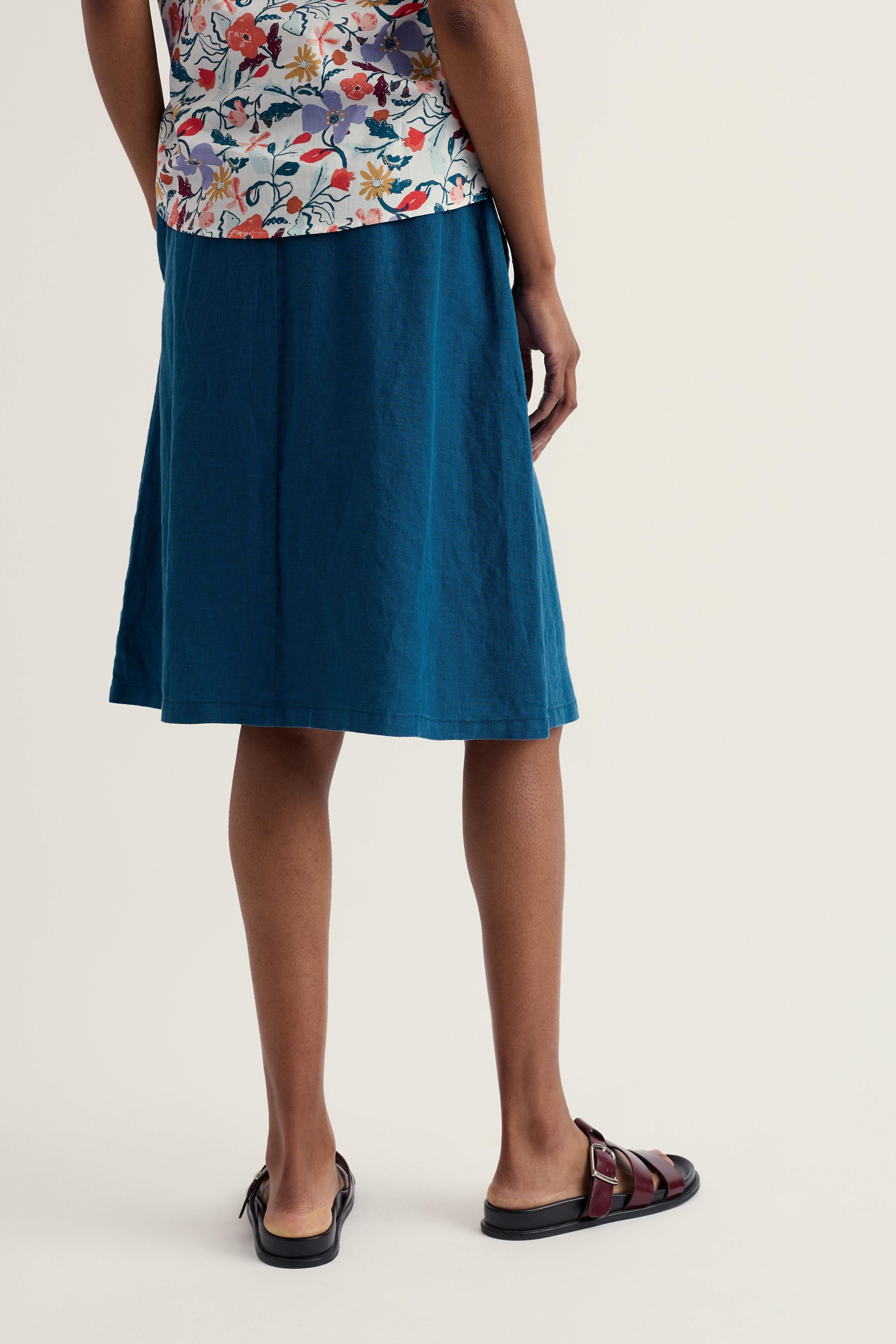 Person wearing a blue skirt and floral top on a plain background
