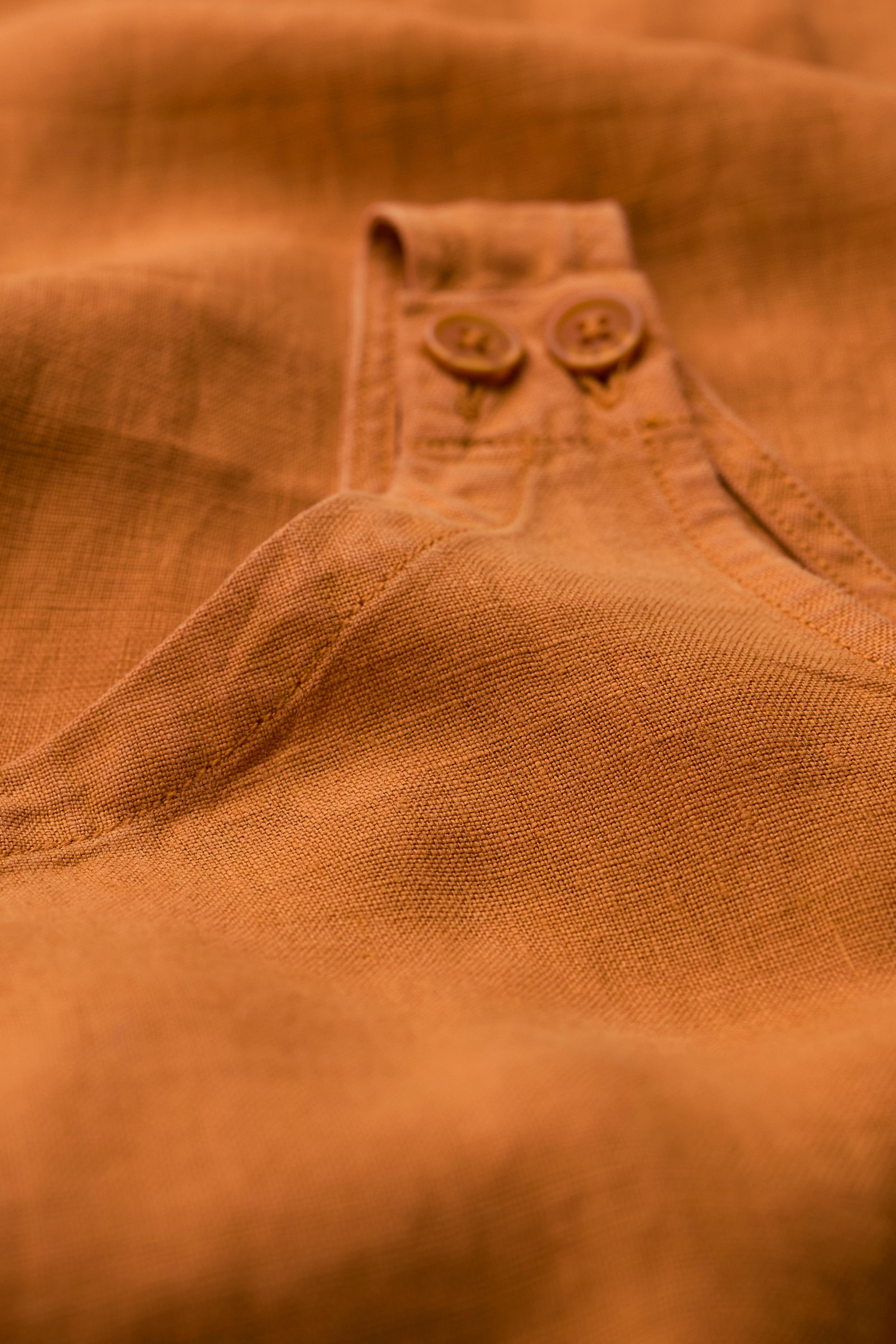 Close-up of a rust orange linen jumpsuit featuring strap details and matching buttons.