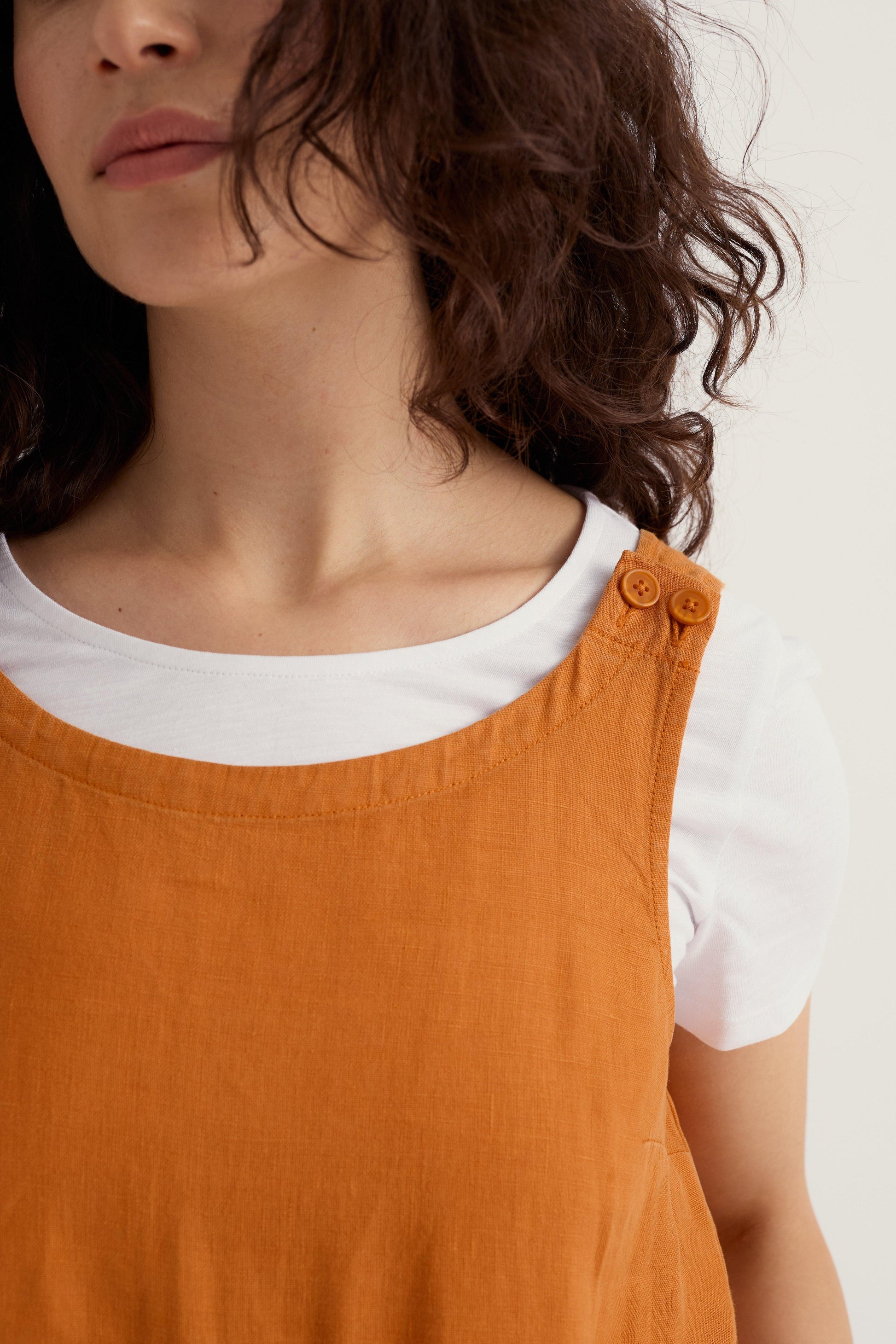 A woman with wavy brown hair wearing an orange linen jumpsuit over a white t-shirt.