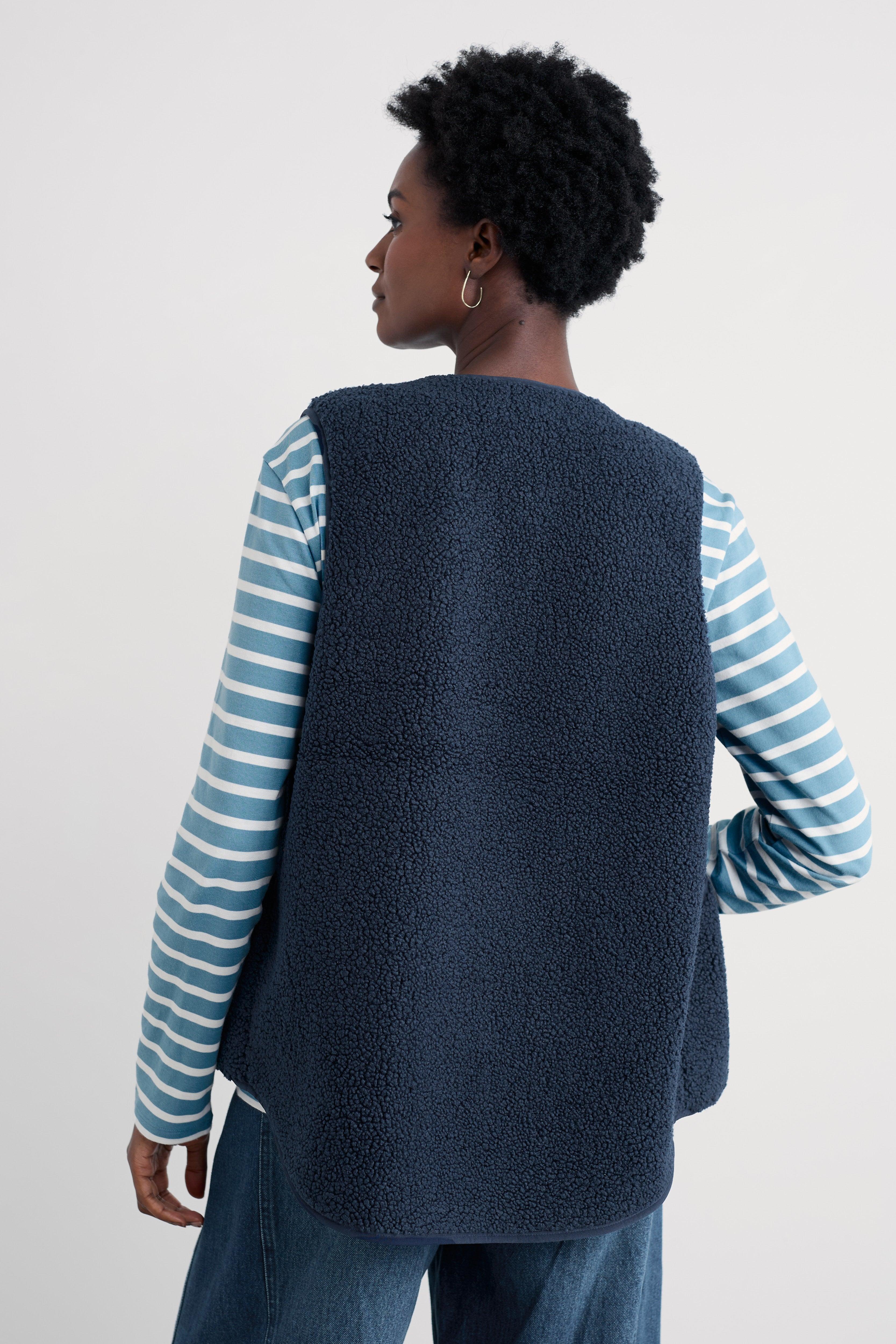 Person wearing a navy blue vest over a striped shirt on a light gray background