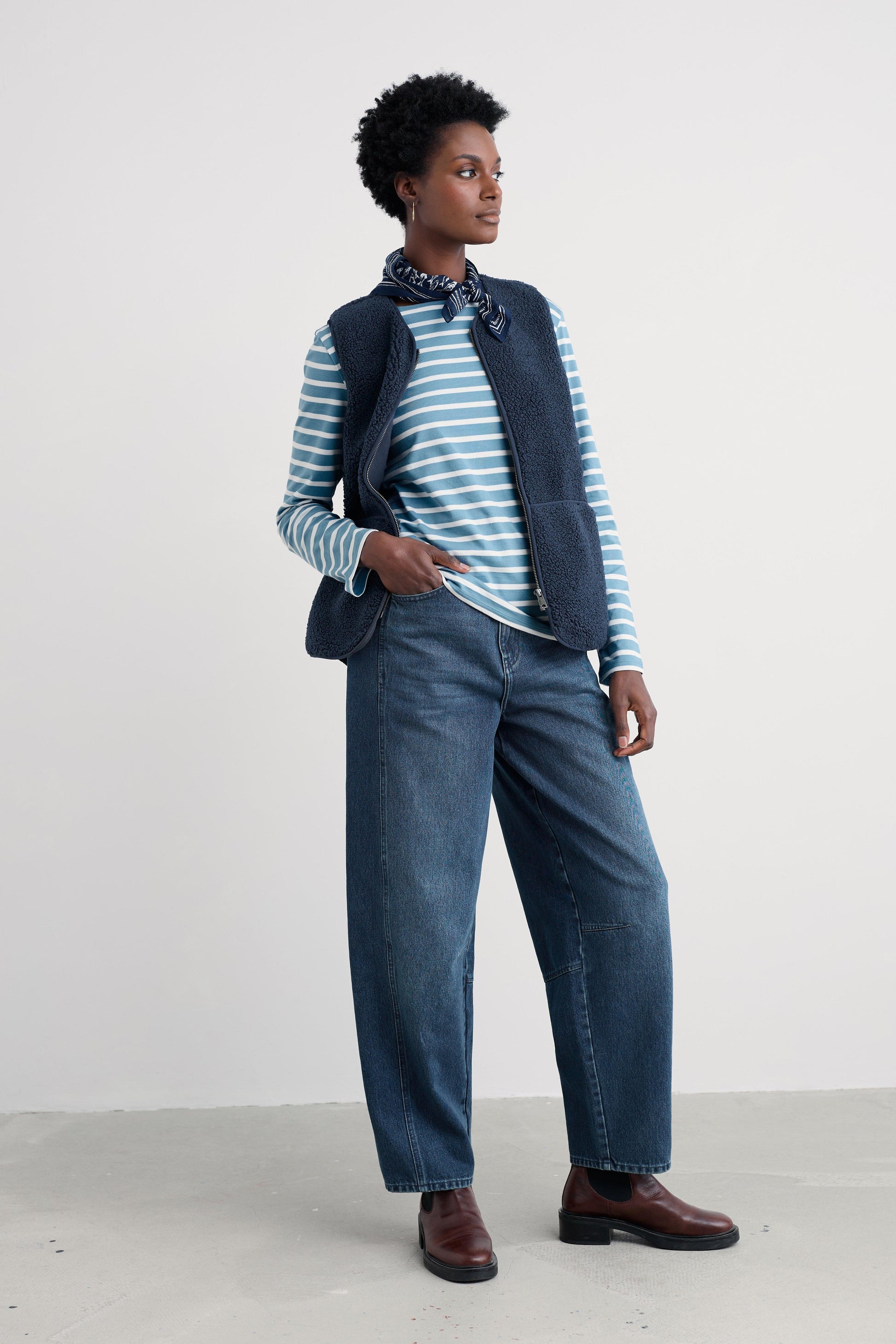 Person wearing a striped sweater, vest, and jeans on a white background